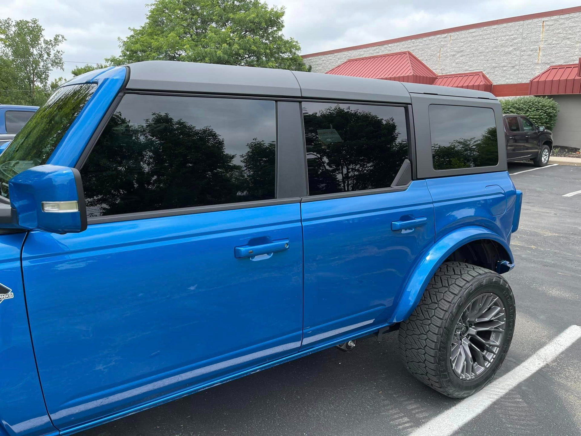 A blue ford bronco is parked in a parking lot in front of a building.