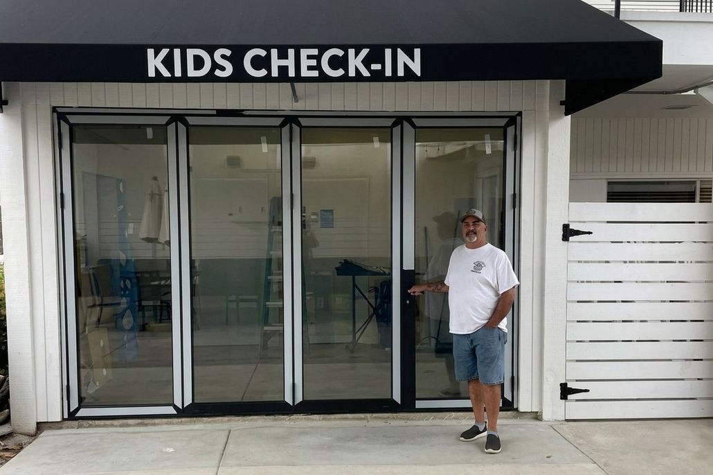 Entrance labeled “KIDS CHECK-IN” with glass doors and a man standing beside it.