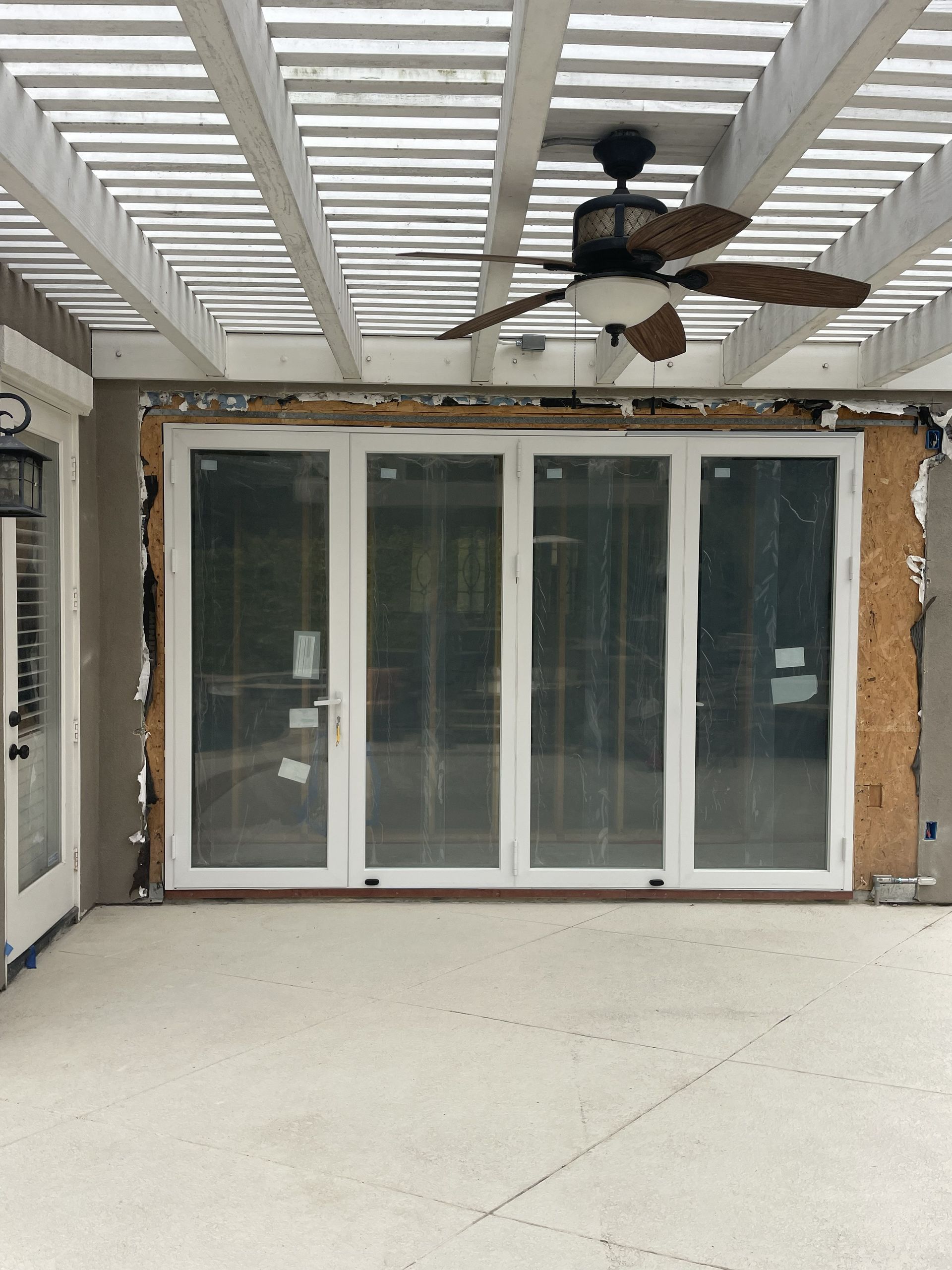 Outdoor patio with large white sliding glass doors under a pergola, ceiling fan overhead