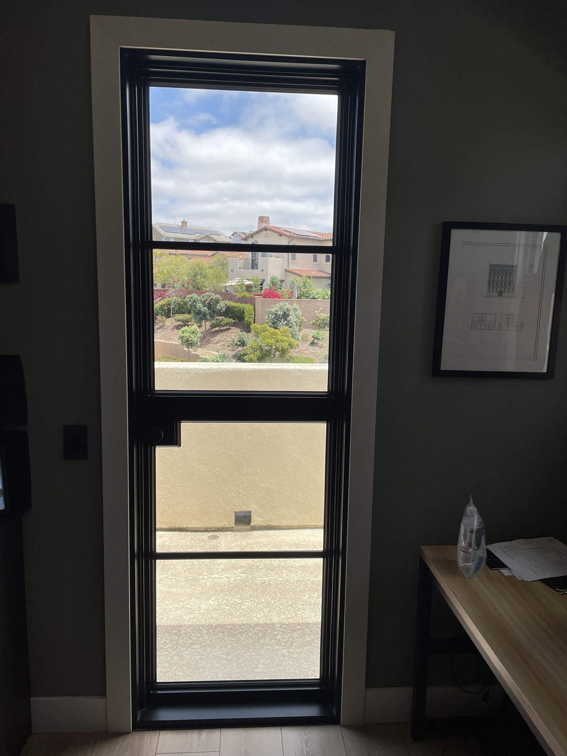 Tall doorway with a glass door leading outside to a courtyard and cloudy sky; framed paper and table at right