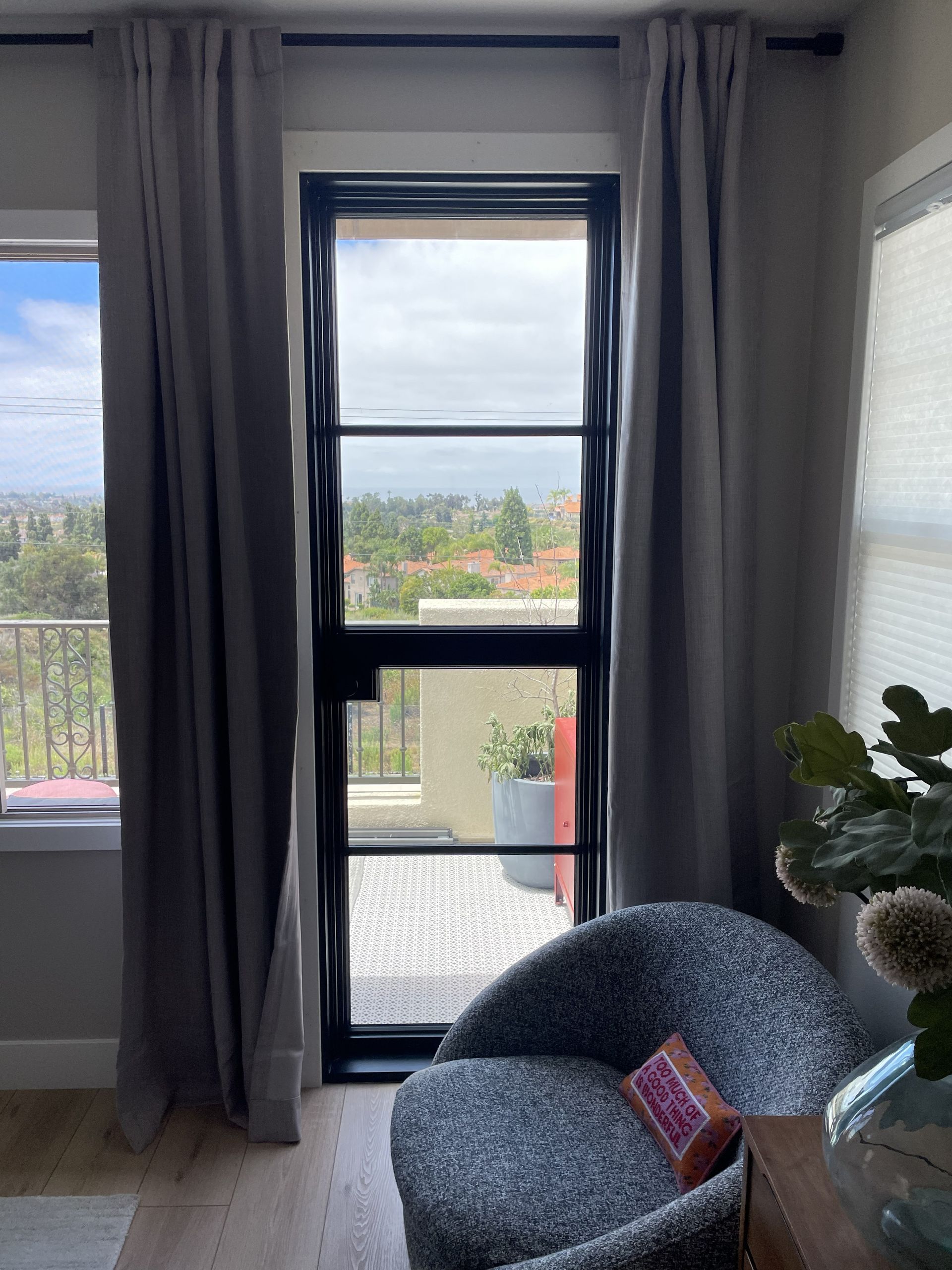 Living room with a large window, gray curtains, and a blue chair with a plant nearby.