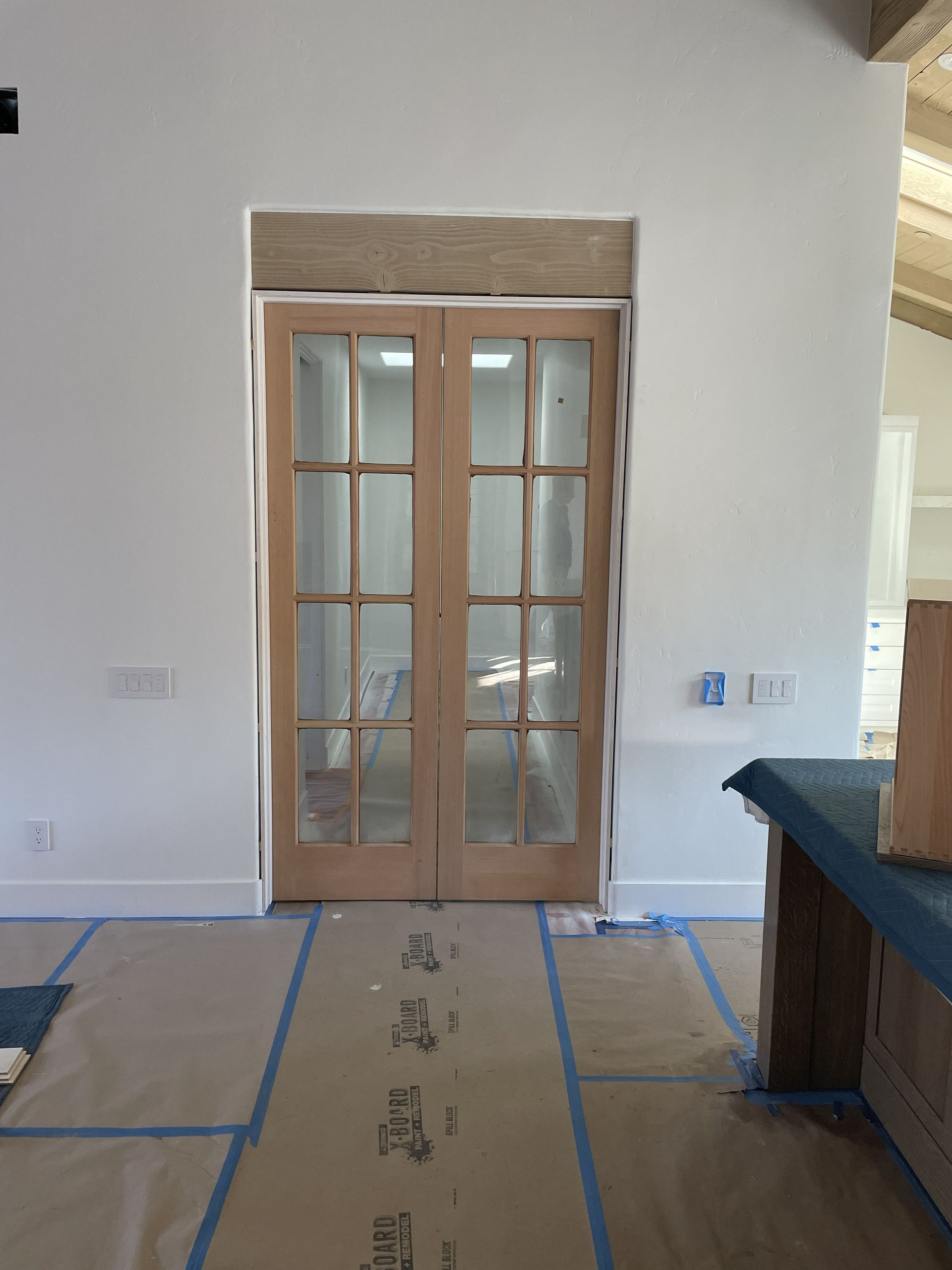 Interior doorway with wooden French doors, wall patching, and blue tape marking the floor