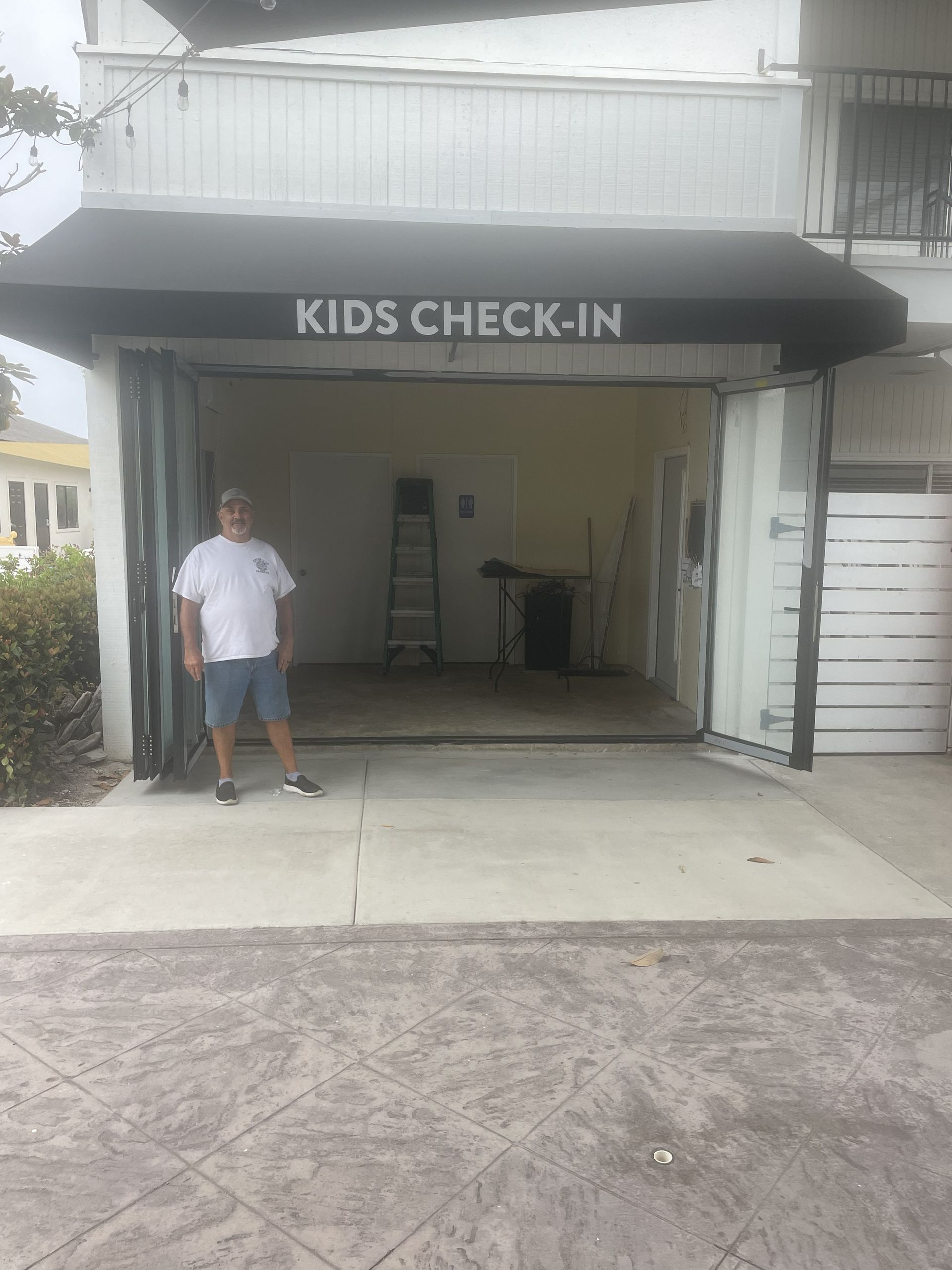 Covered driveway entrance labeled “Kids Check-In” with a person standing at the left side.