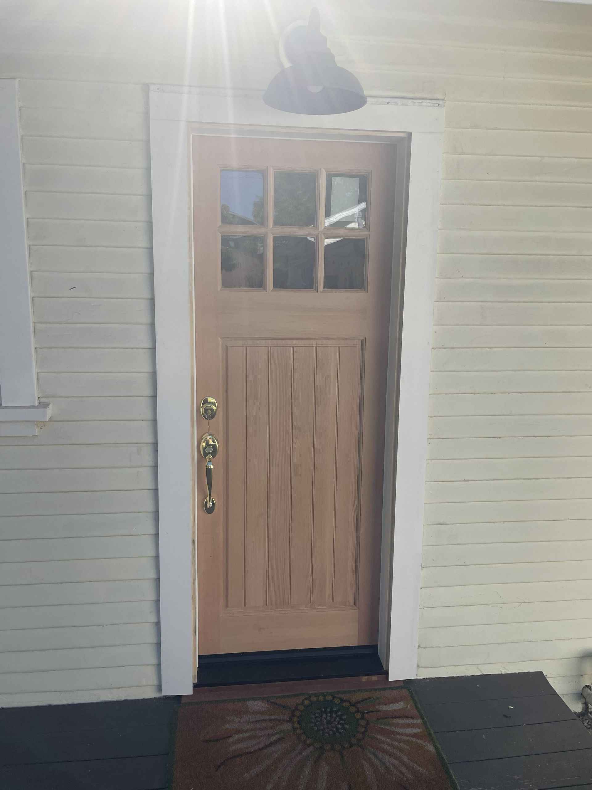 Wooden front door with small window panes and a black porch light on a brick exterior wall.