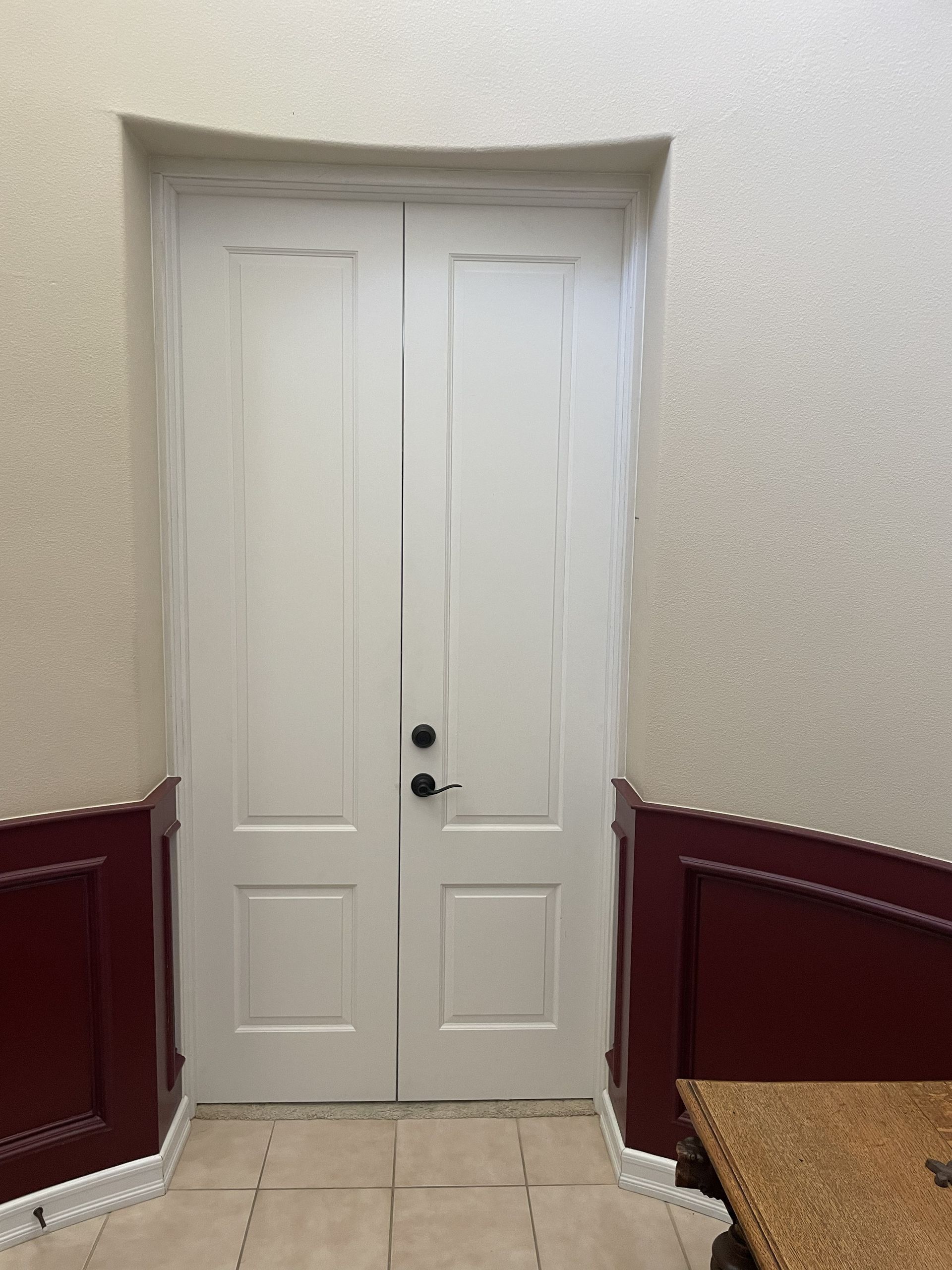 White double doors in a narrow hallway with red wainscoting and beige walls.