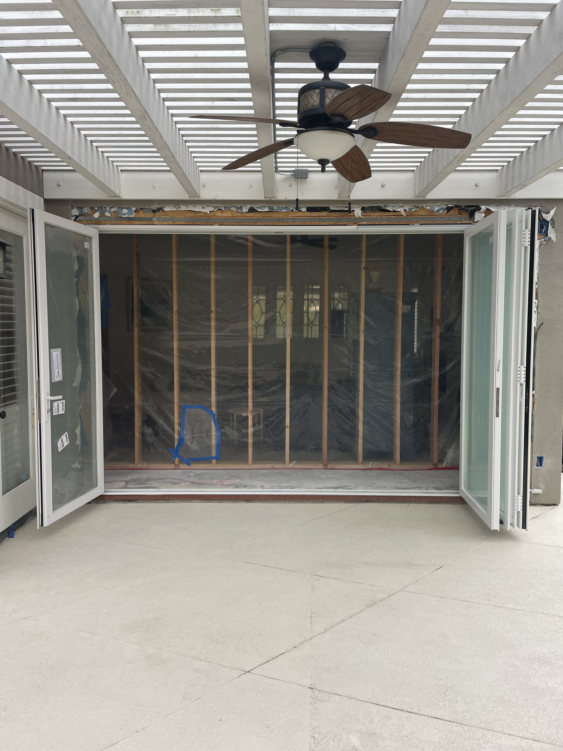 Open patio with white screens, exposed wall framing, ceiling fan, and concrete floor