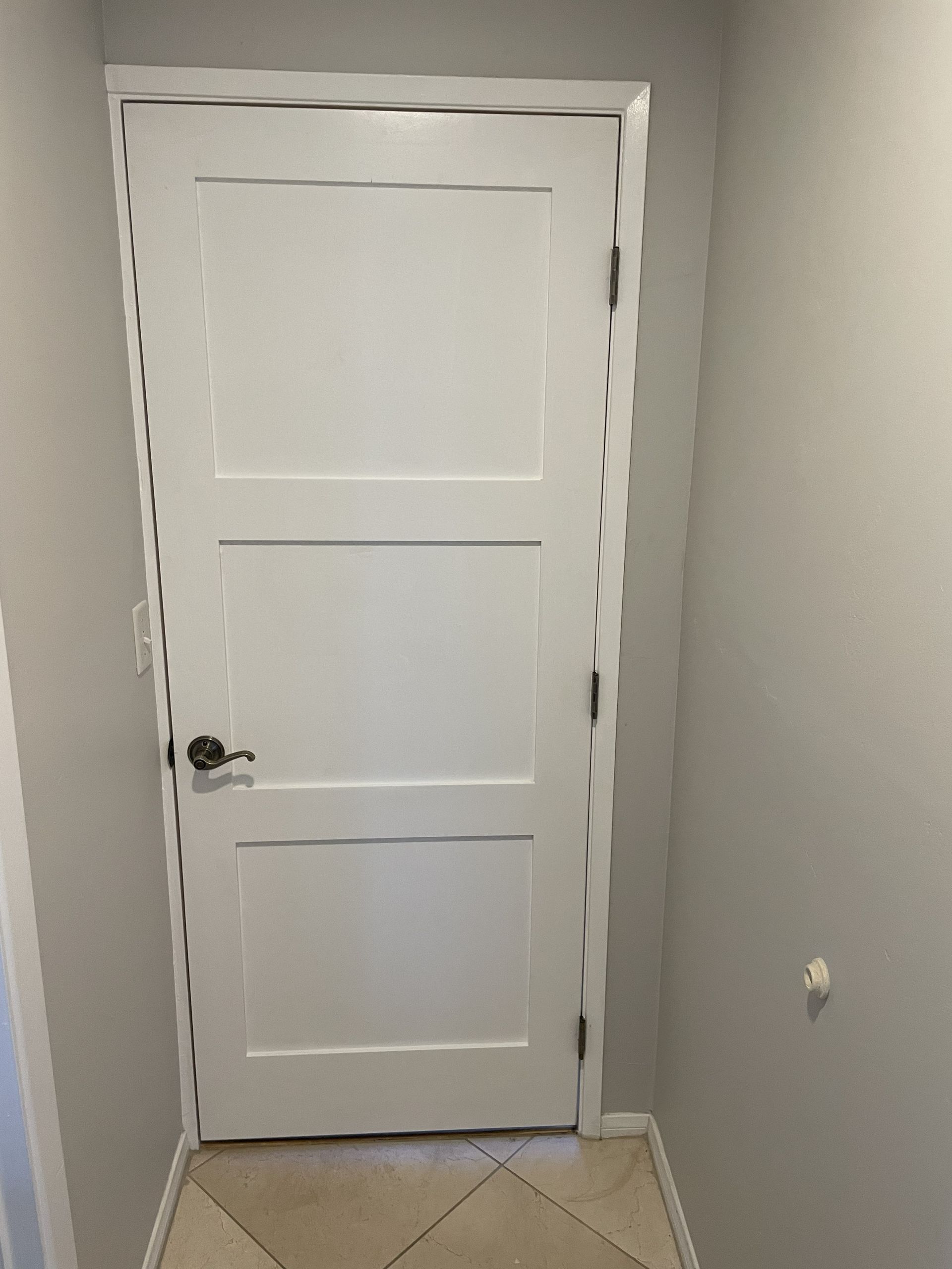 Closed white interior door in a narrow hallway with gray walls and beige floor trim.