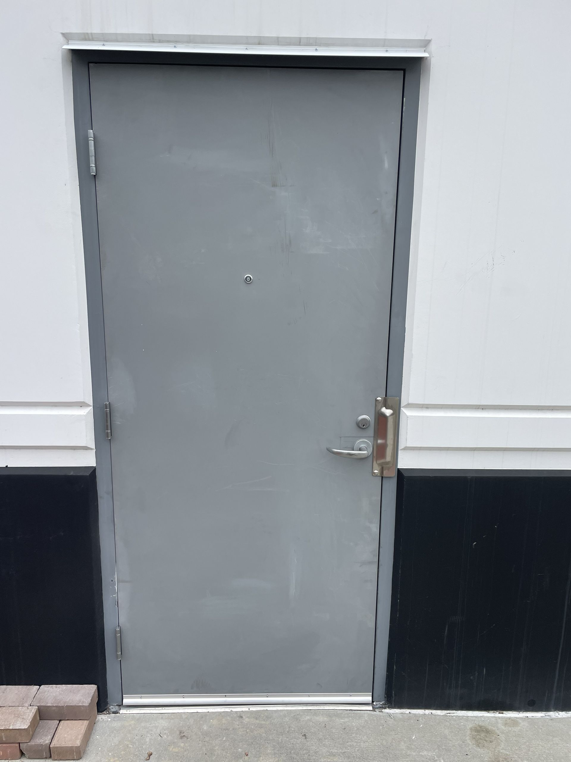 Gray metal door in a white-and-black wall, with a silver handle and deadbolt.