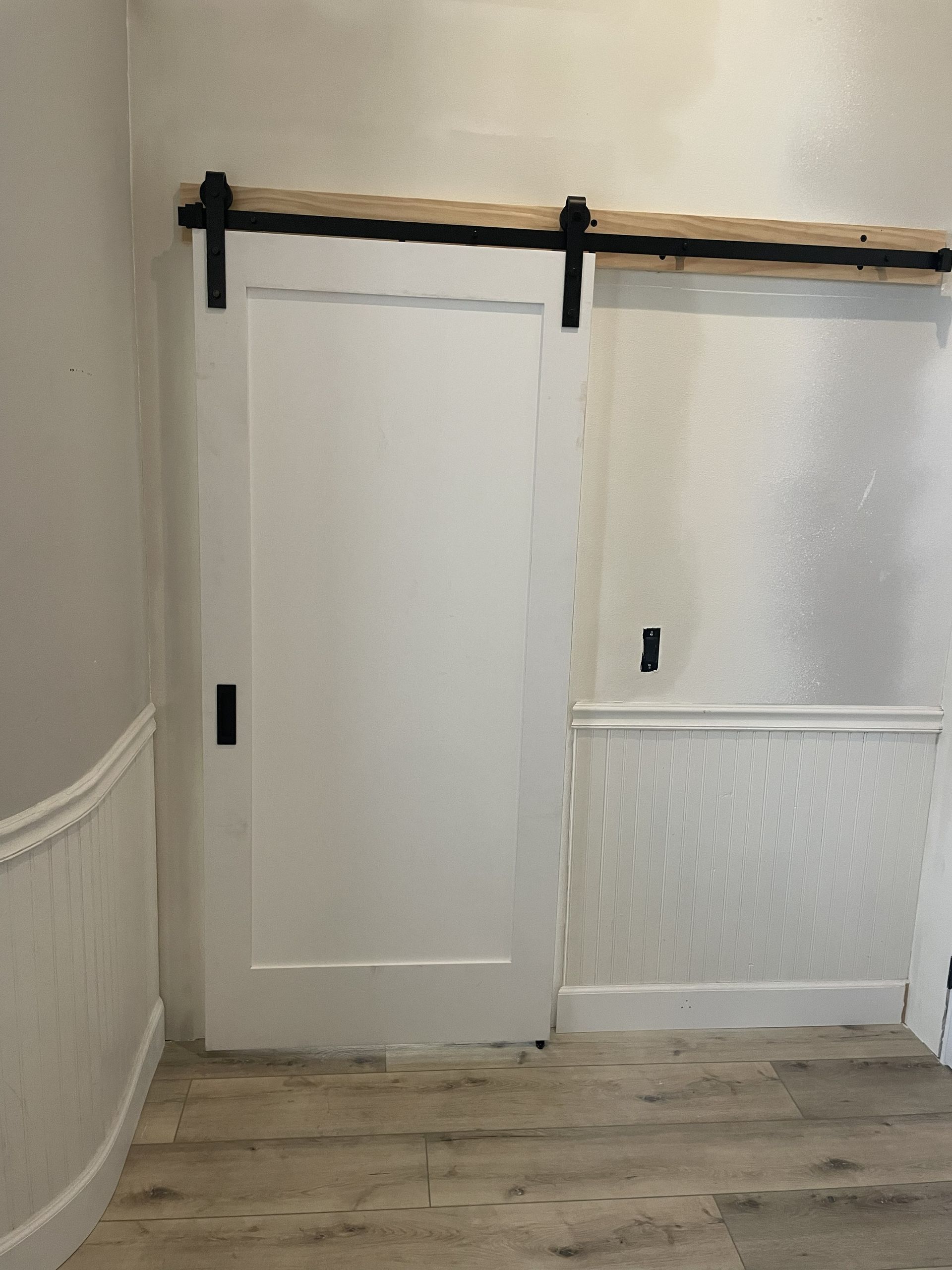 White sliding barn door with black hardware in a hallway over light wood flooring.