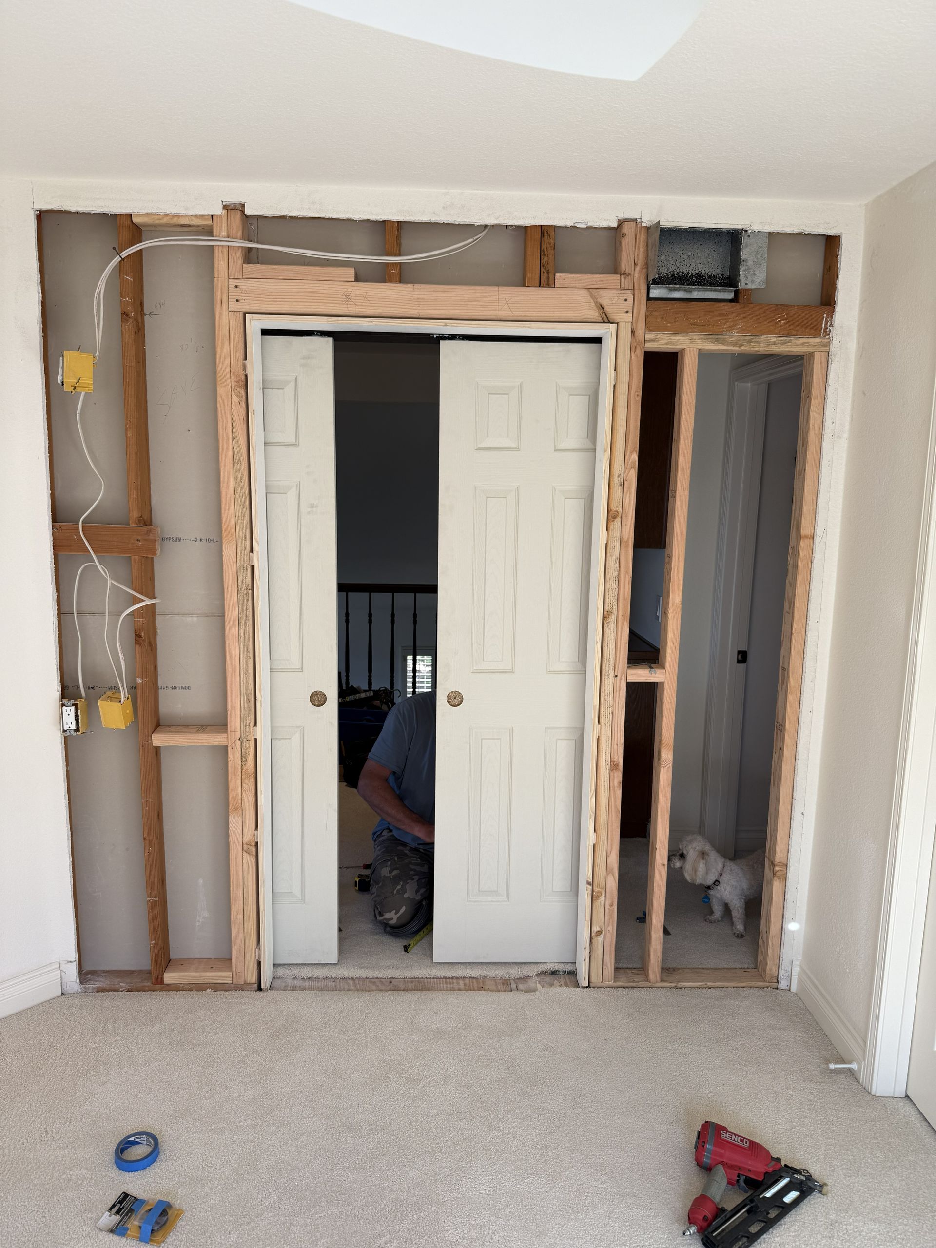 Interior wall under renovation with open framing around a double closet doorway and tools on the floor