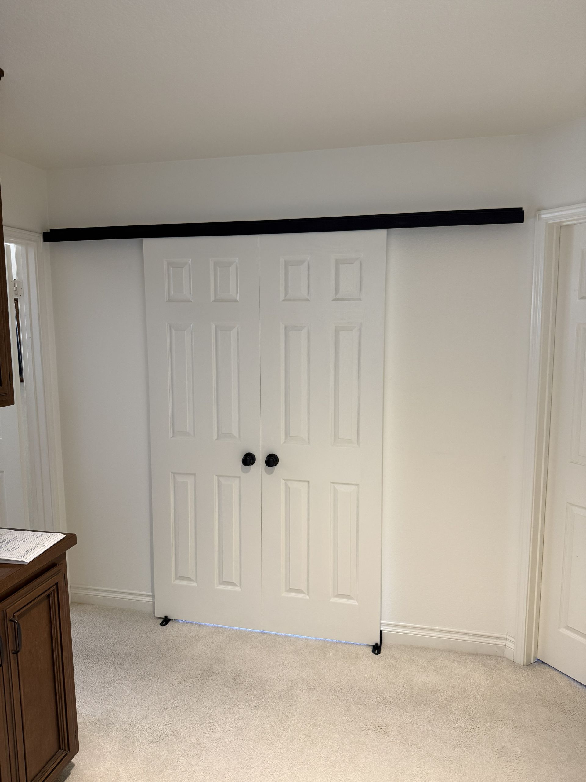 White double closet doors in a carpeted room with curtains on either side and a dresser at left.
