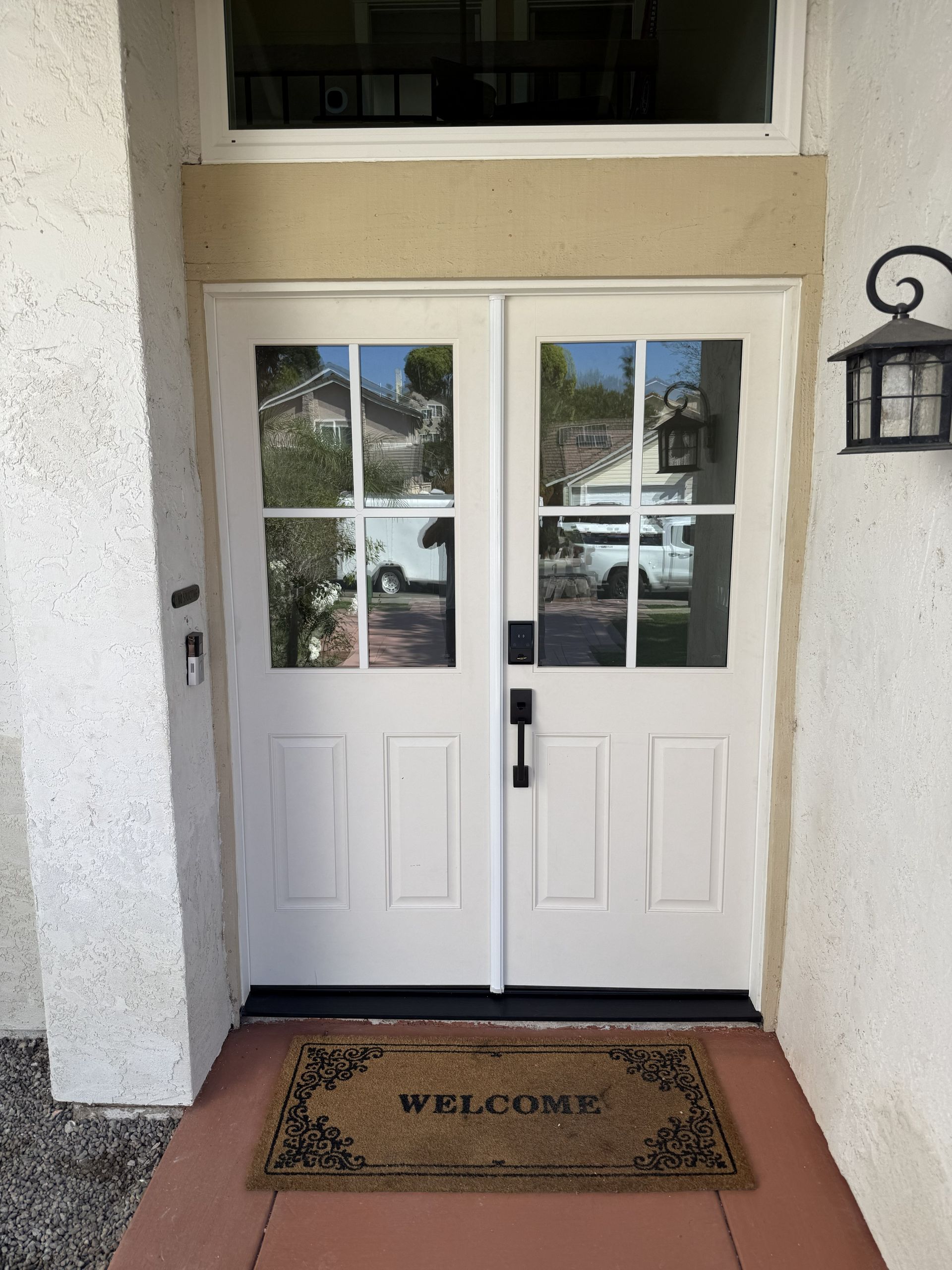 White double front doors with windows and a welcome mat at a building entrance.