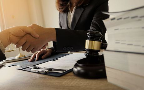 A lawyer is shaking hands with a client in front of a judge 's gavel.