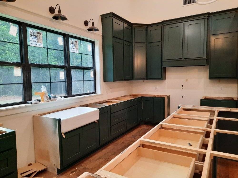 A kitchen under construction with green cabinets and a white sink.