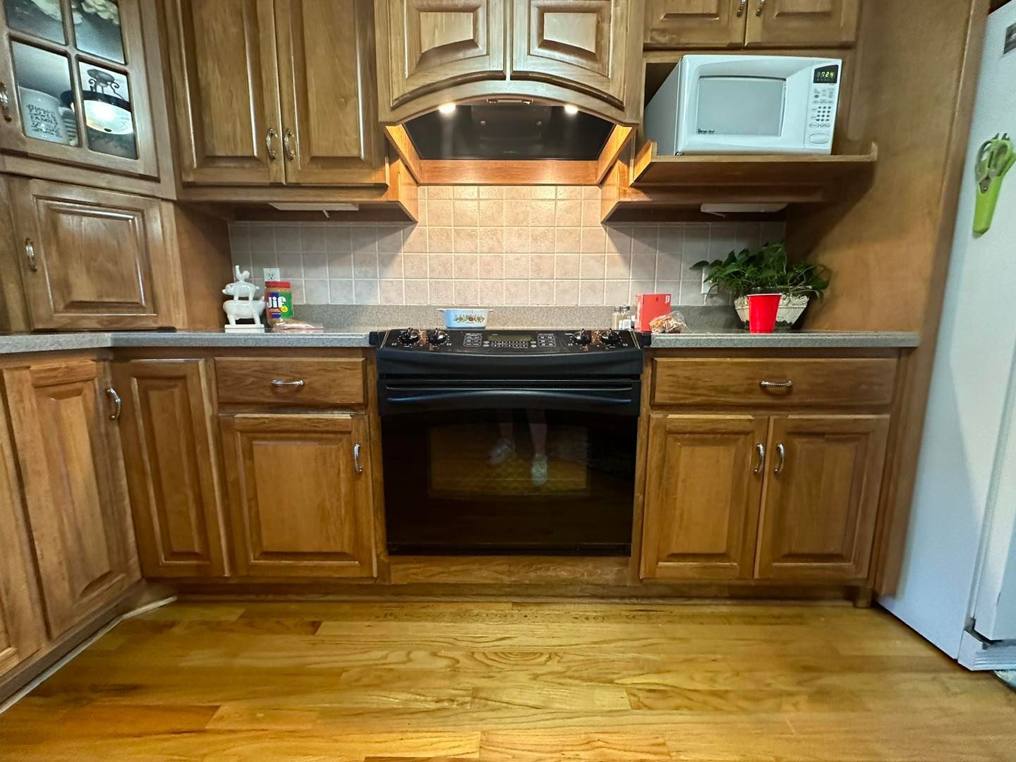 A kitchen with wooden cabinets , a stove , a microwave , and a refrigerator.
