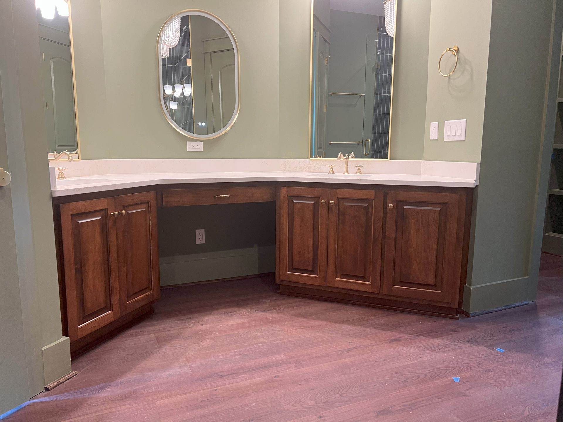 Vanity with dark wood cabinets, a white countertop, and two mirrors against a green wall.
