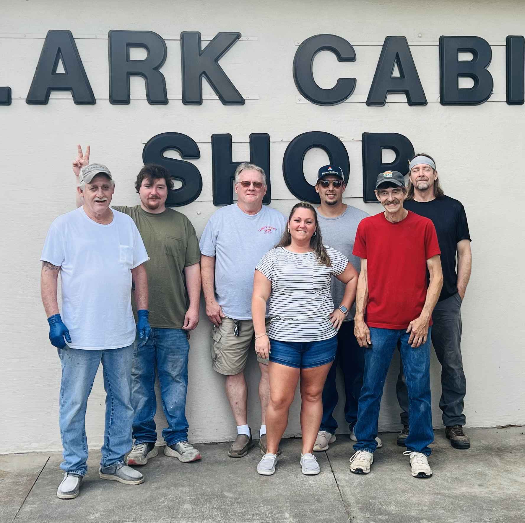 A group of people standing in front of a sign that says Clark cabinet shop.