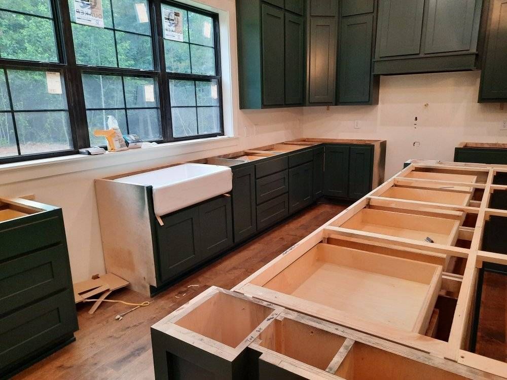 A kitchen under construction with green cabinets and a white sink.
