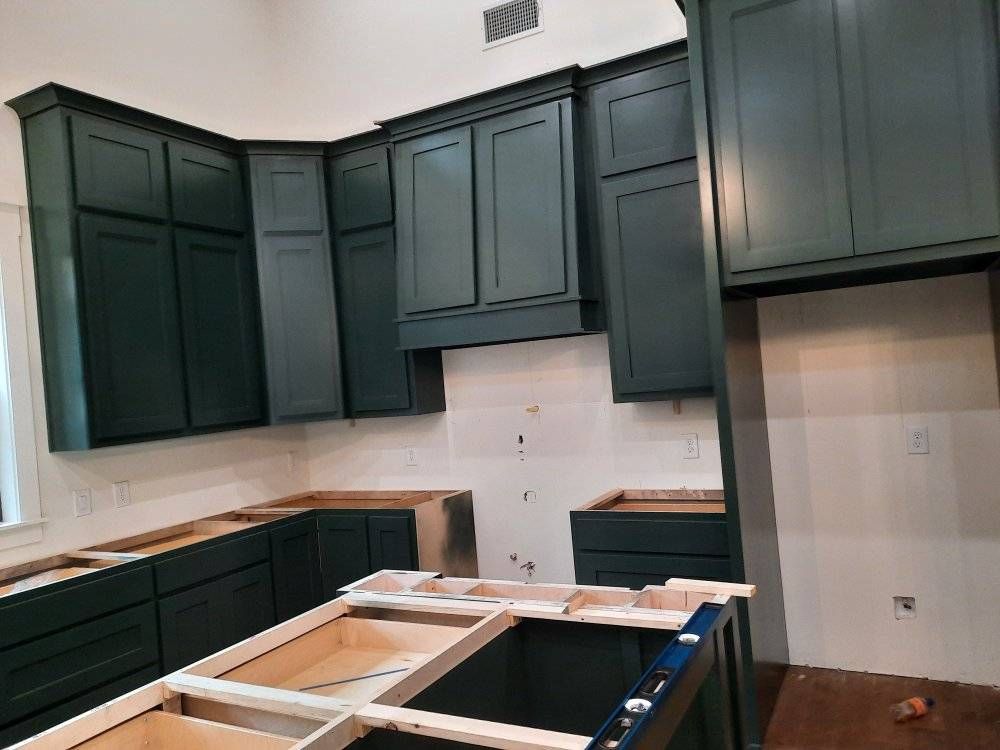 A kitchen with green cabinets and black counter tops is being built.