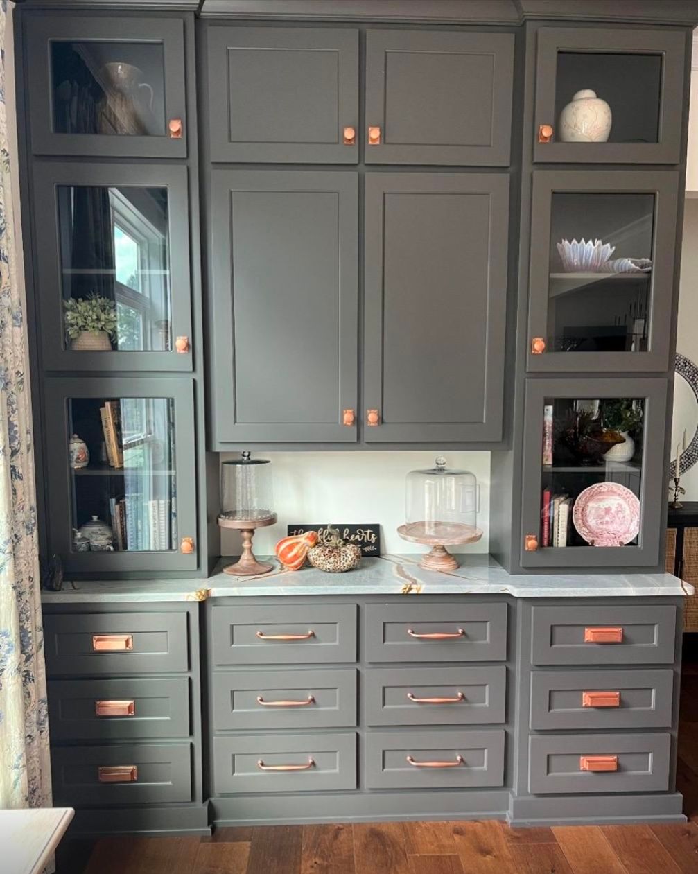 A kitchen with gray cabinets, drawers, and glass doors.