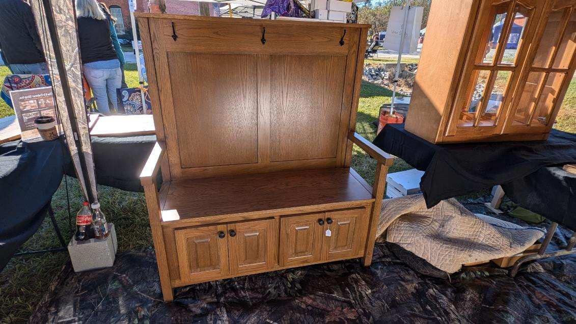 A wooden bench with drawers and hooks is sitting on the ground at a flea market.