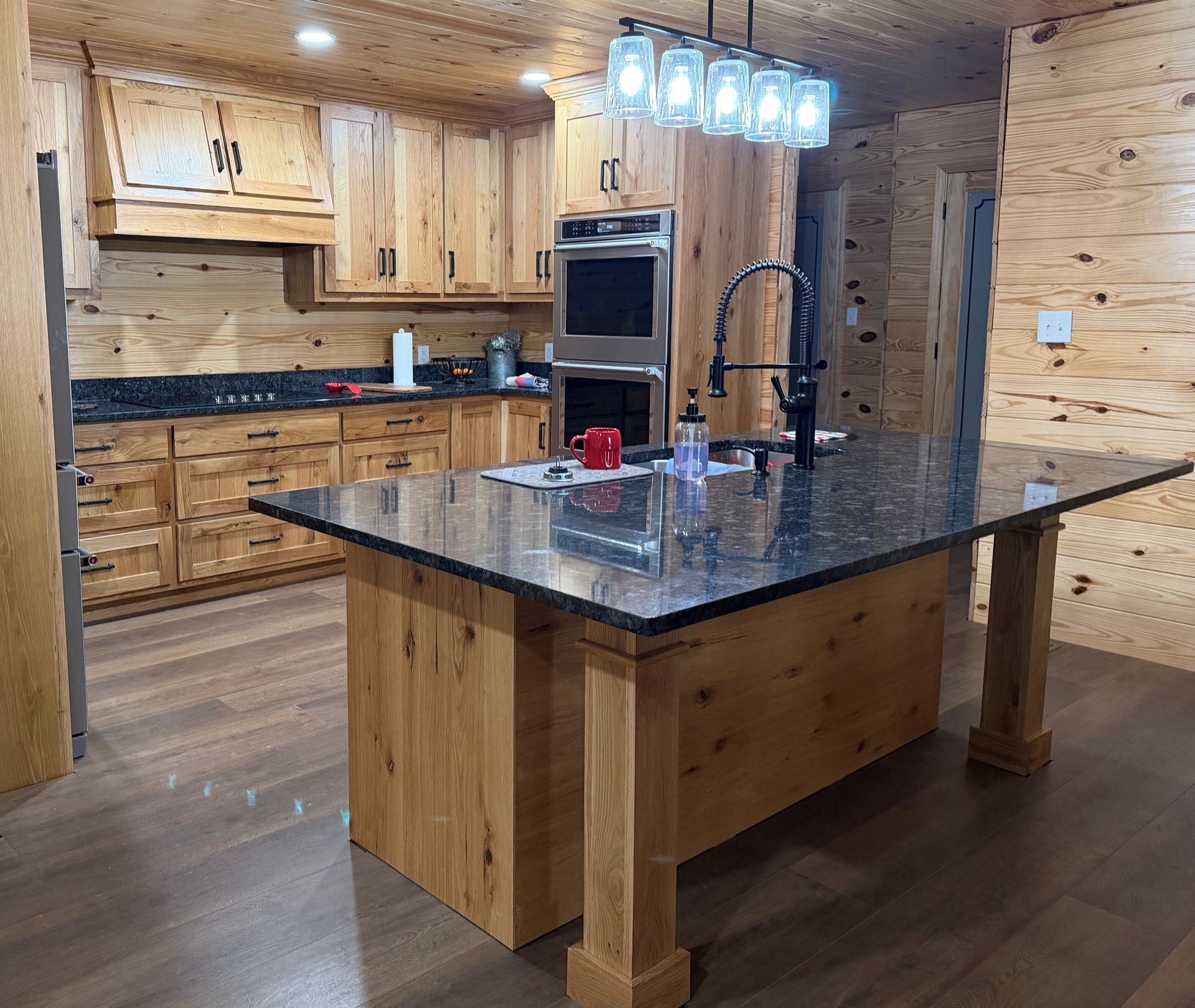 Wooden kitchen with a large dark granite island, pendant lights, and stainless steel appliances.