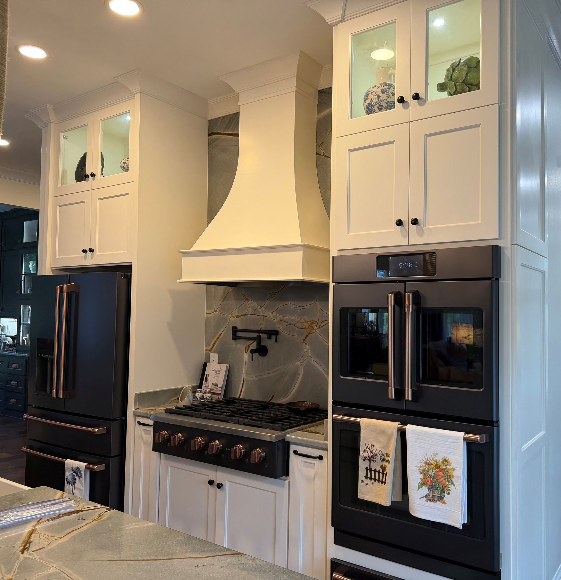 Bright white kitchen with black appliances, a central stove and range hood, and glass-front upper cabinets.