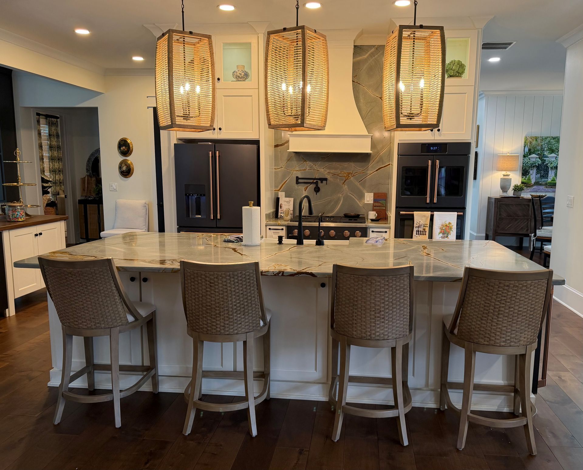 Modern kitchen with marble island, four woven stools, and hanging pendant lights