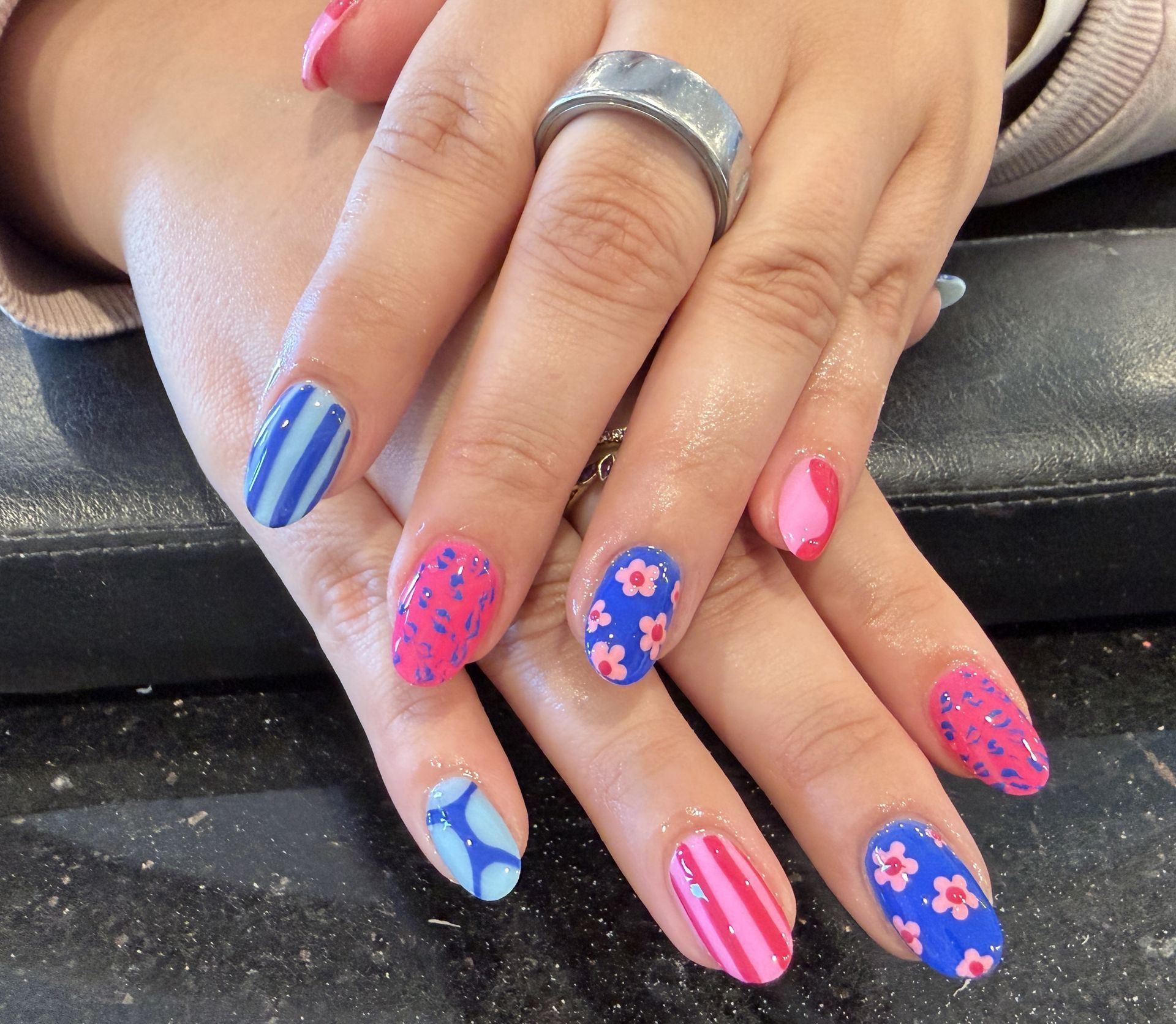 Hands with colorful blue, pink, and floral nail art resting on a black surface.