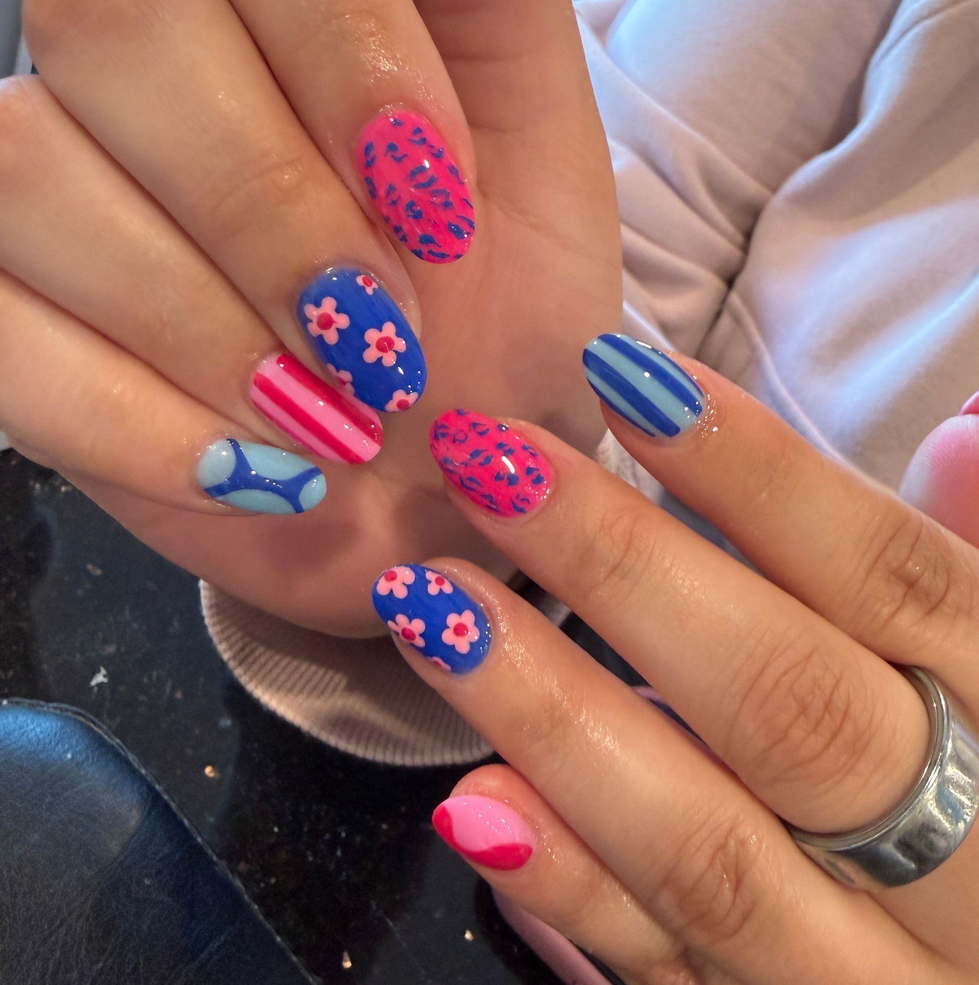 Hands showing colorful blue, pink, and neon floral nail art with stripes and abstract patterns