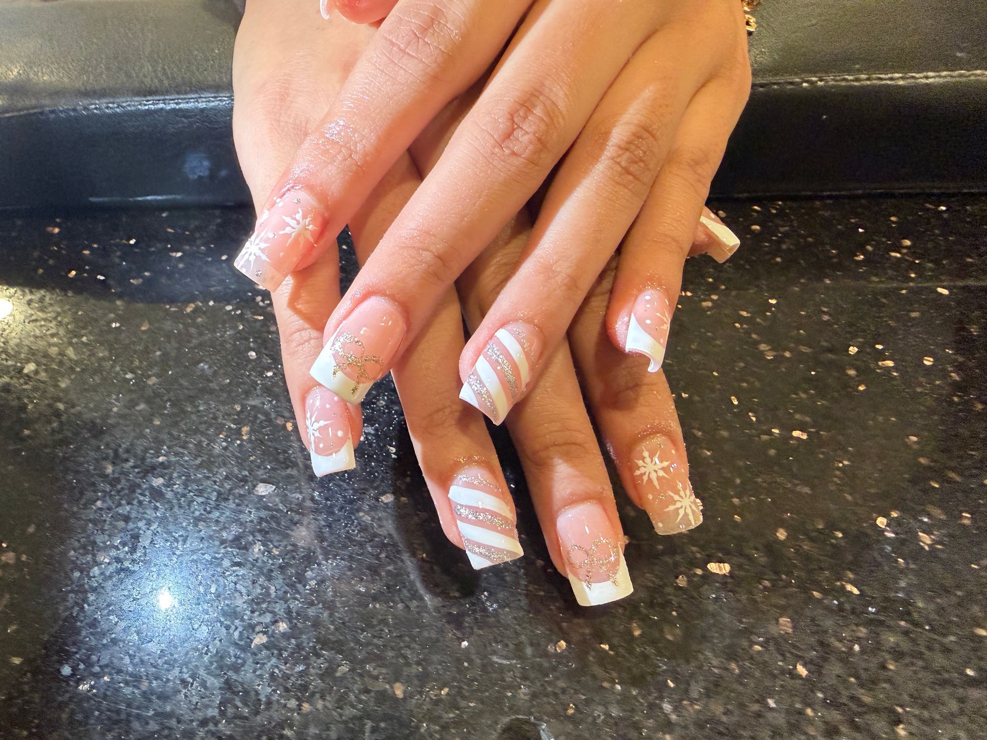 Hands with pink-and-white nail art resting on a black speckled countertop
