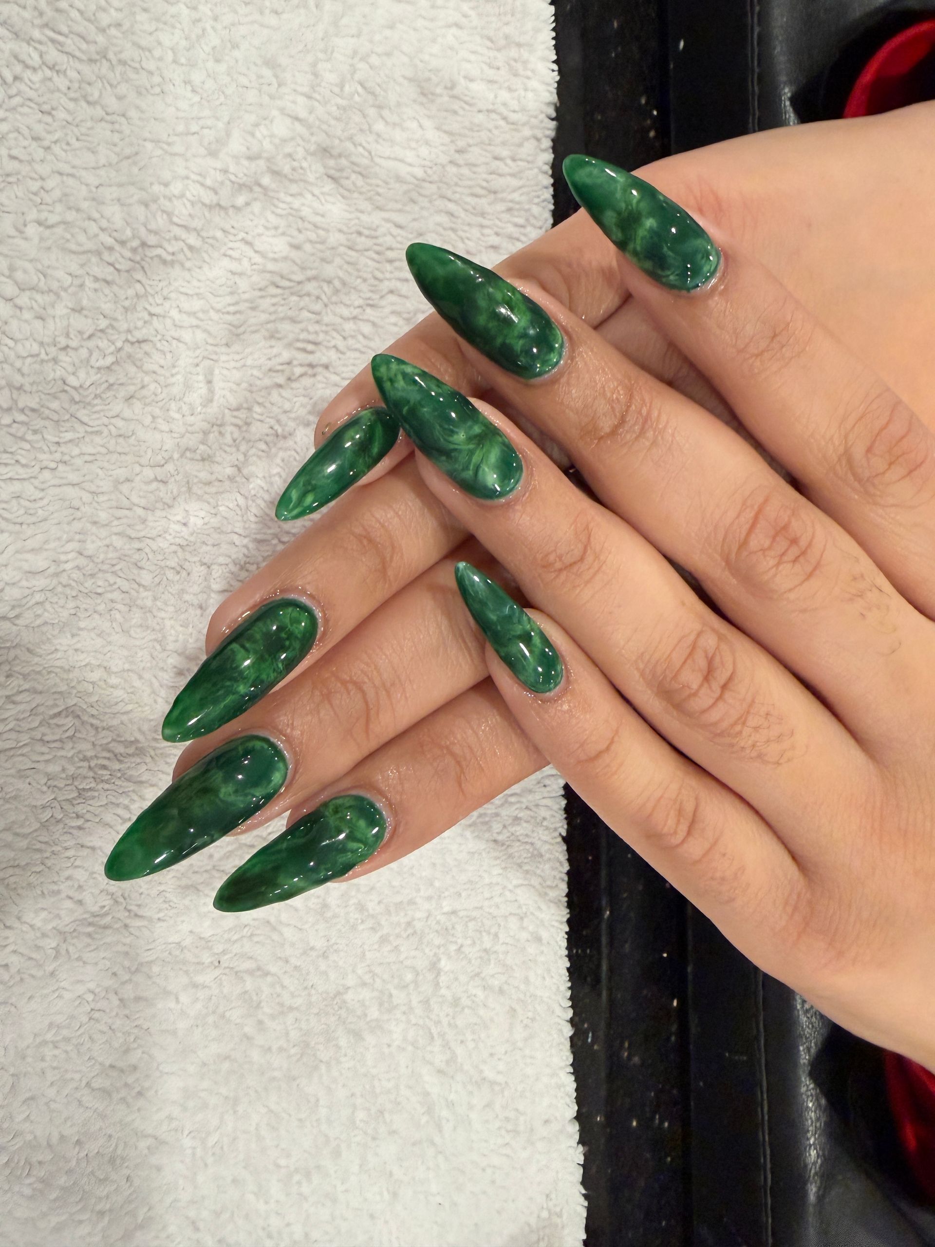 Hands with long, glossy emerald-green stiletto nails resting on a towel.