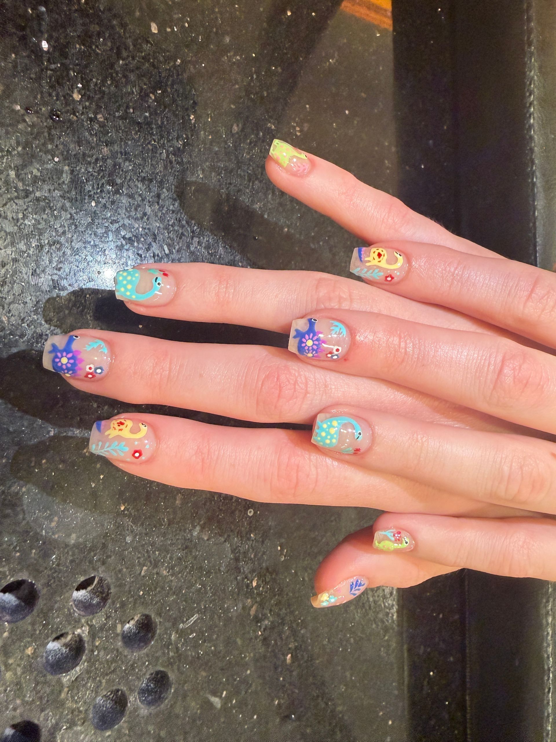 Hands with colorful jeweled nail art resting on a dark countertop.