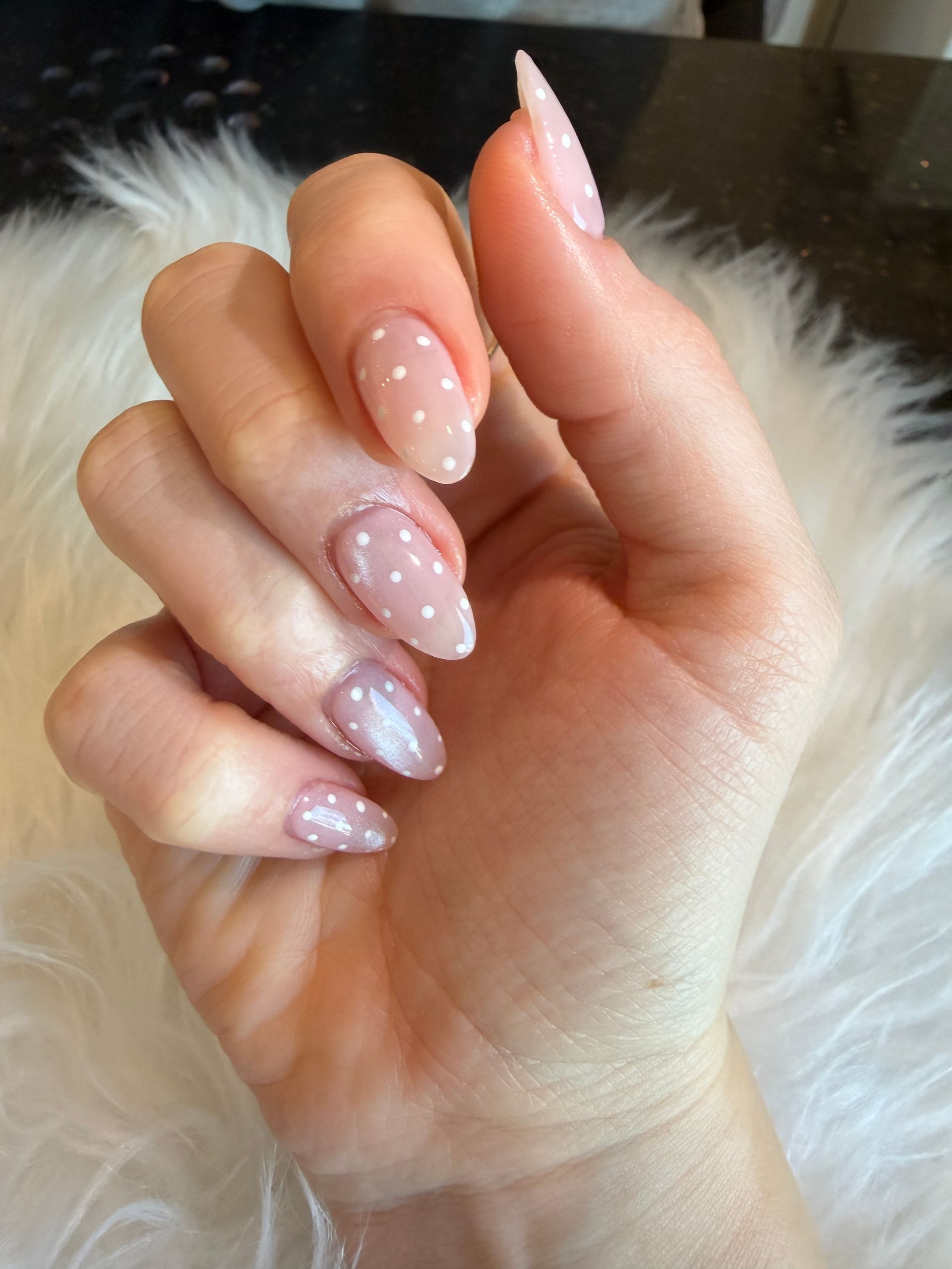 Hand with long pink glitter nails and white polka dots on a fluffy white background