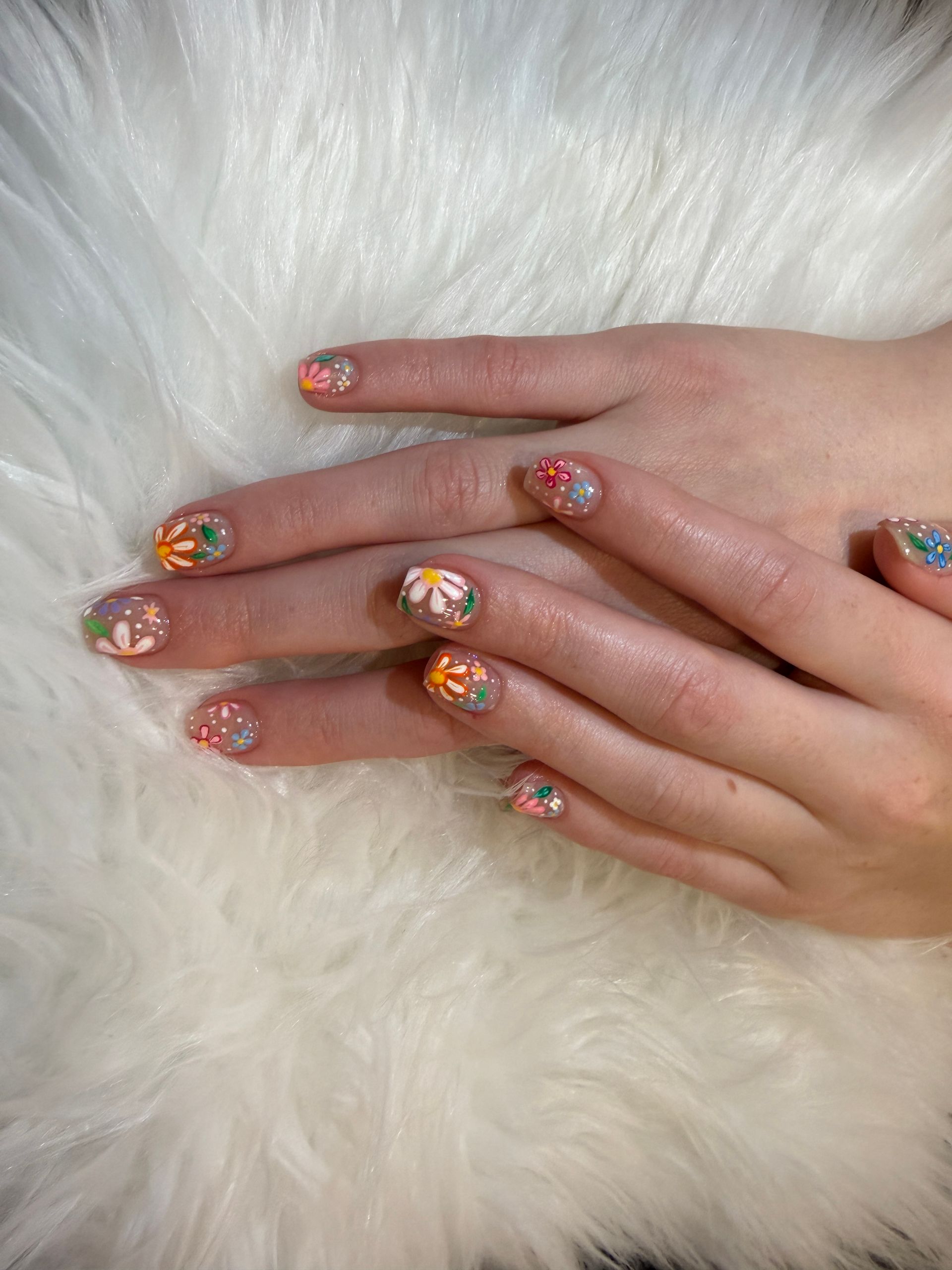Hands with colorful glitter nail art resting on a white faux fur background