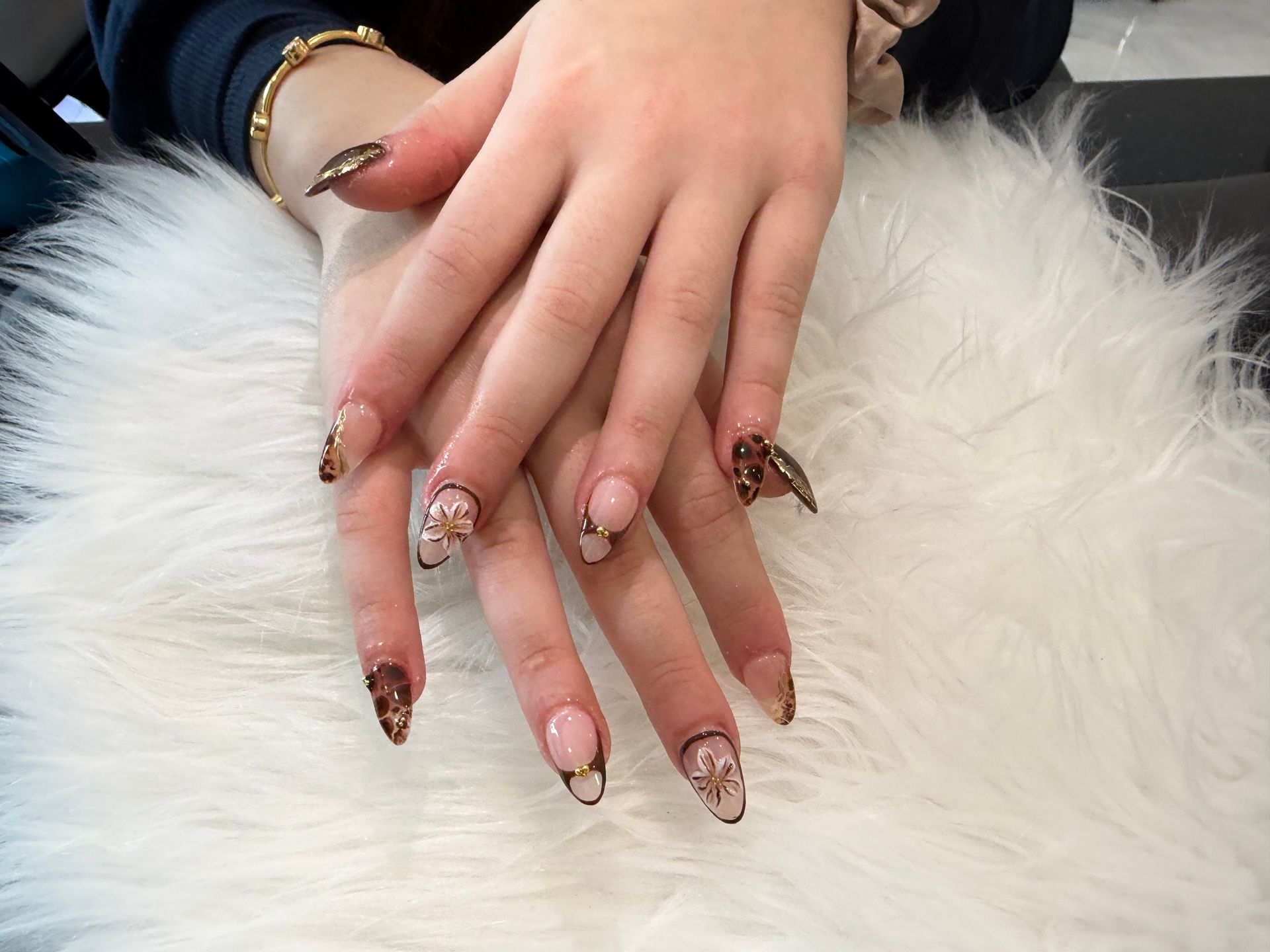 Hands with long decorated nails resting on a white fluffy surface.