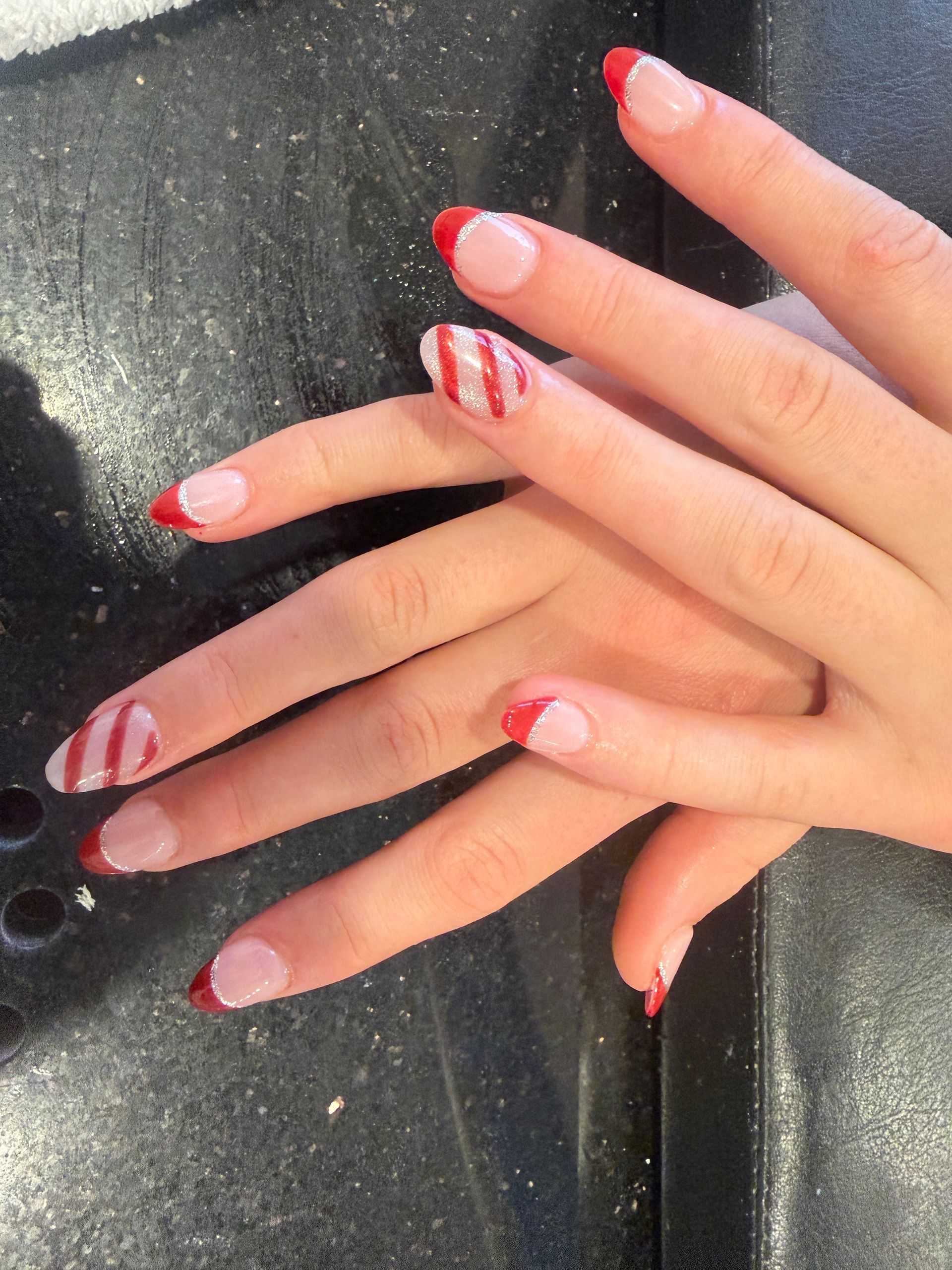 Hands with red-and-white striped French-tip nails resting on a dark textured surface