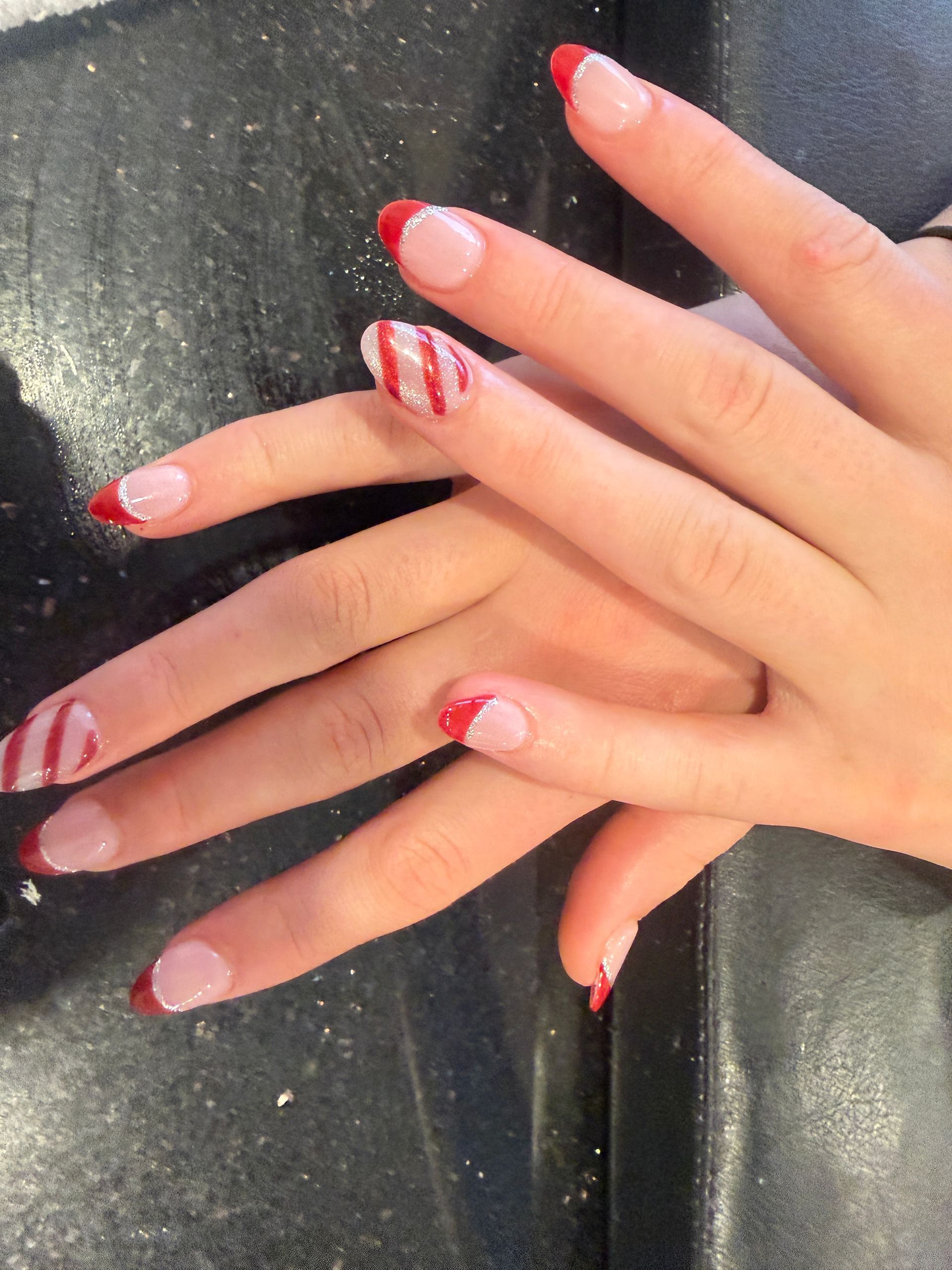 Close-up of hands with pink and white striped manicured nails on a dark surface