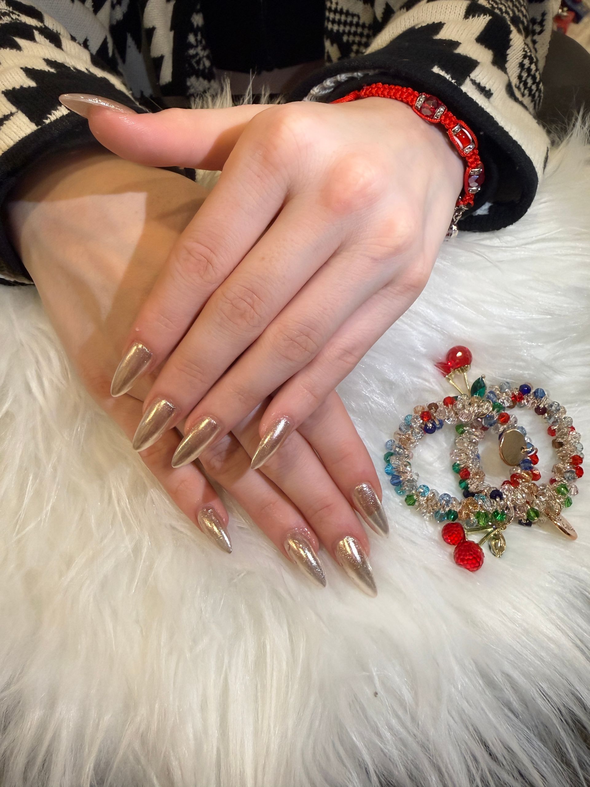Manicured hand with gold nails resting on white fur beside a jeweled brooch and black-and-cream sweater sleeve