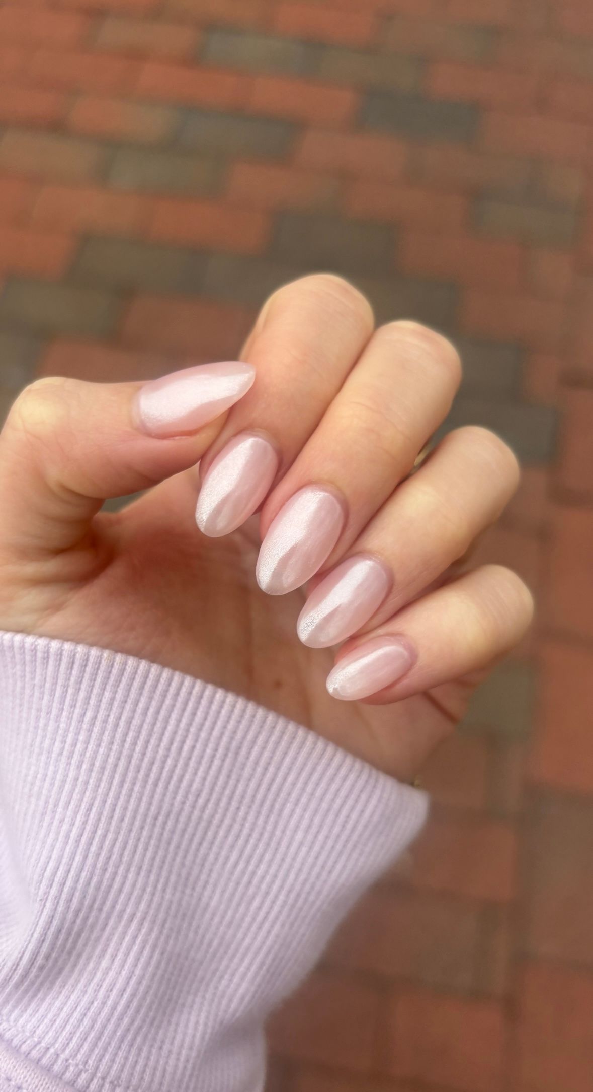 Hand with pale pink manicured nails against a blurred brick background