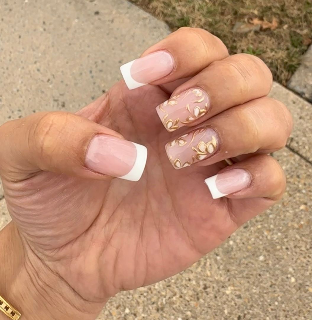 Hand with French manicure and gold floral nail art, held over a sidewalk outdoors