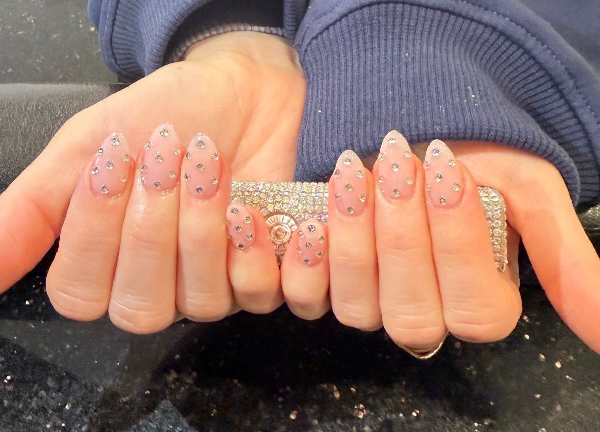 Hands holding a glittery silver clutch, showing long pink glitter nails.