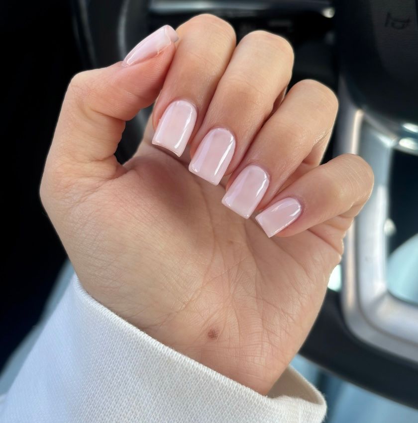 Close-up of a hand with glossy pale pink manicured nails in a car interior