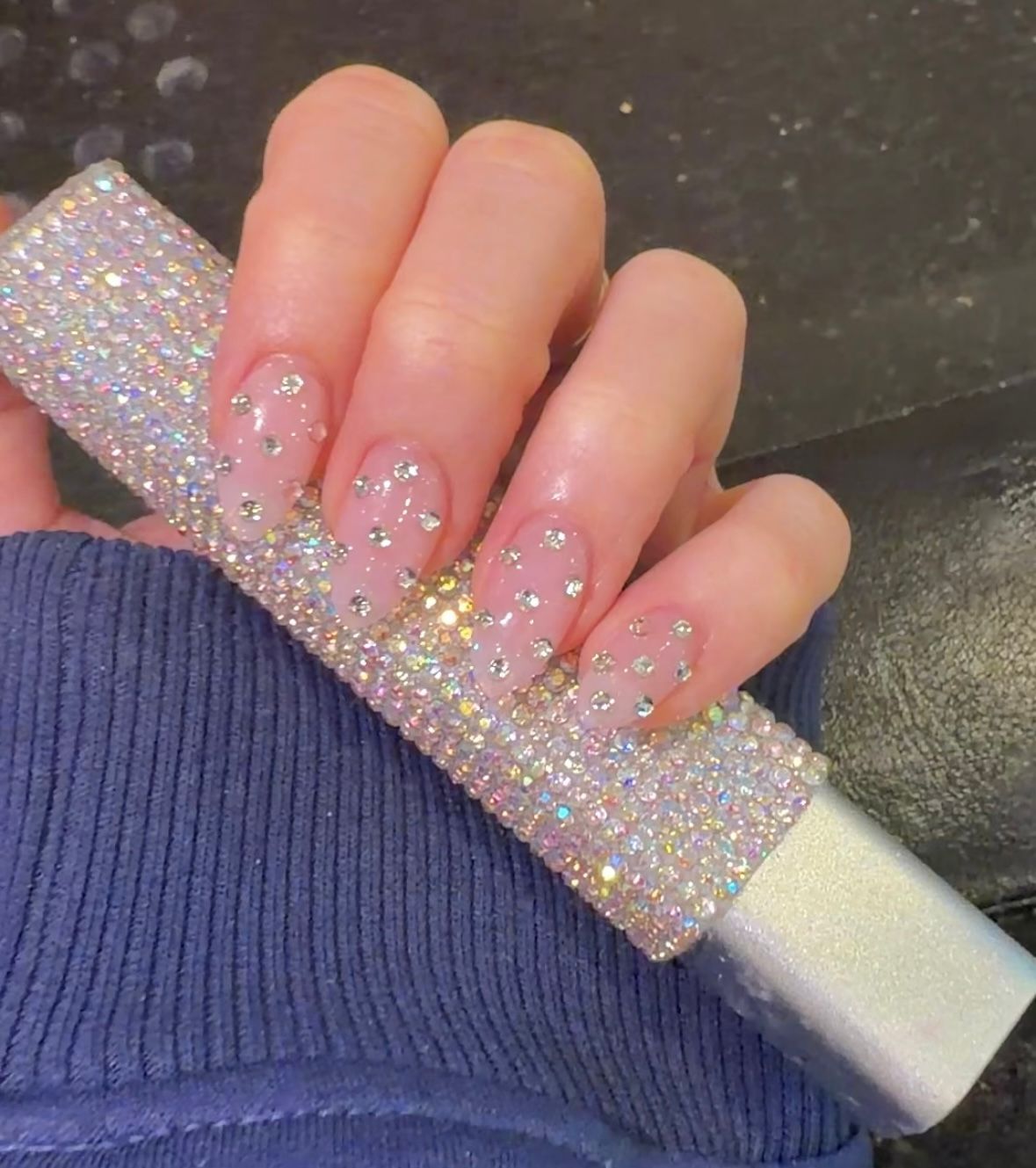 Hand with glittery pink nails holding a rhinestone-covered nail file over a dark tabletop
