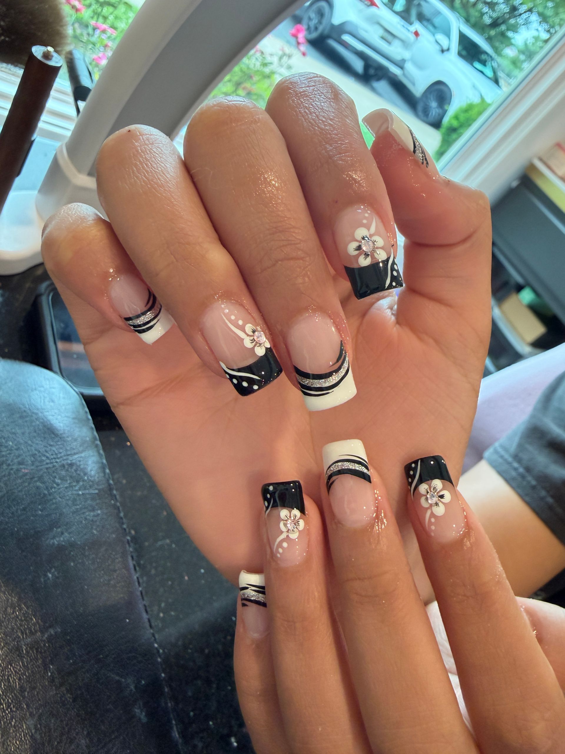 Hands with black-and-white French tip nail art and glitter accents, shown close up indoors.
