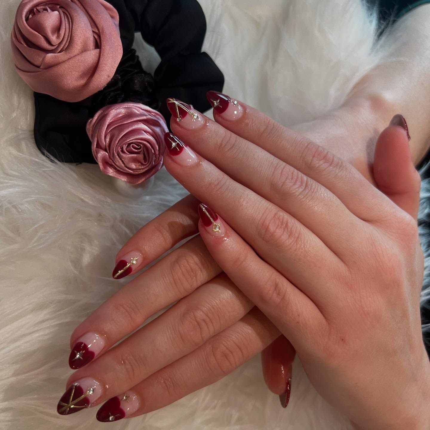 Hands with burgundy and clear nail design, placed next to a black scrunchie with pink roses.