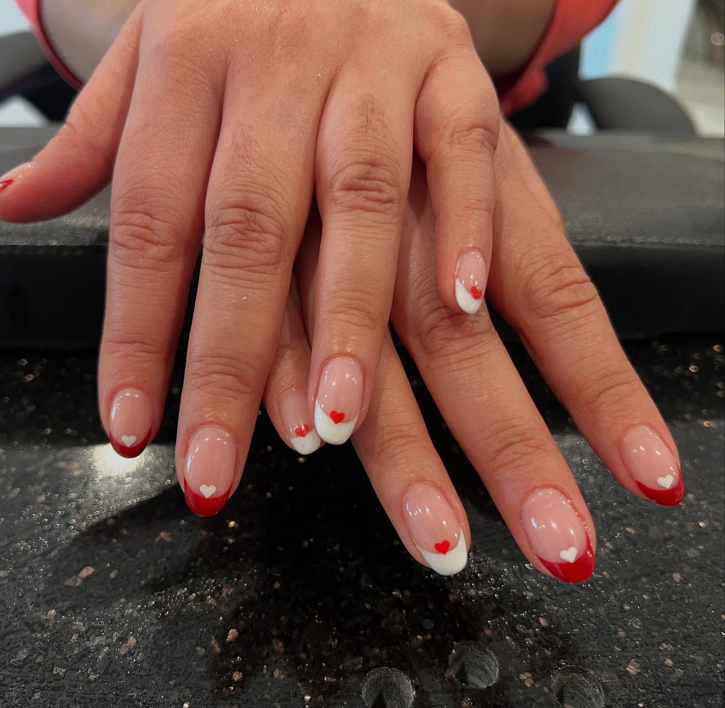 Hands with oval-shaped nails featuring a clear base and red heart tips.