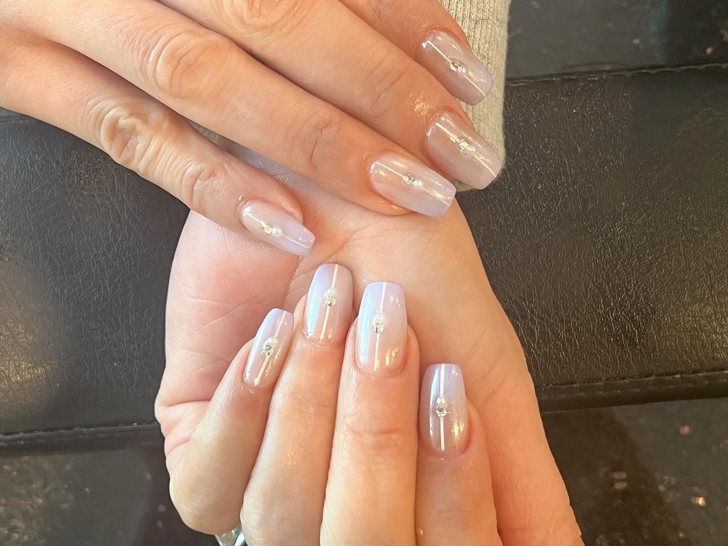 Hands with light purple, rectangular nails, adorned with silver embellishments.