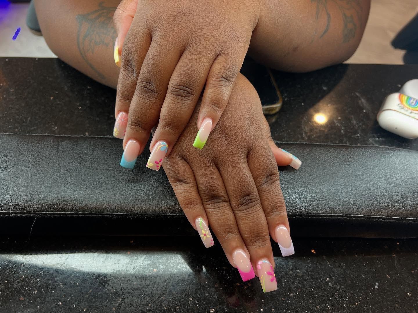 Hands with colorful square-shaped acrylic nails, gradient pink and white with pastel tips on a black surface.