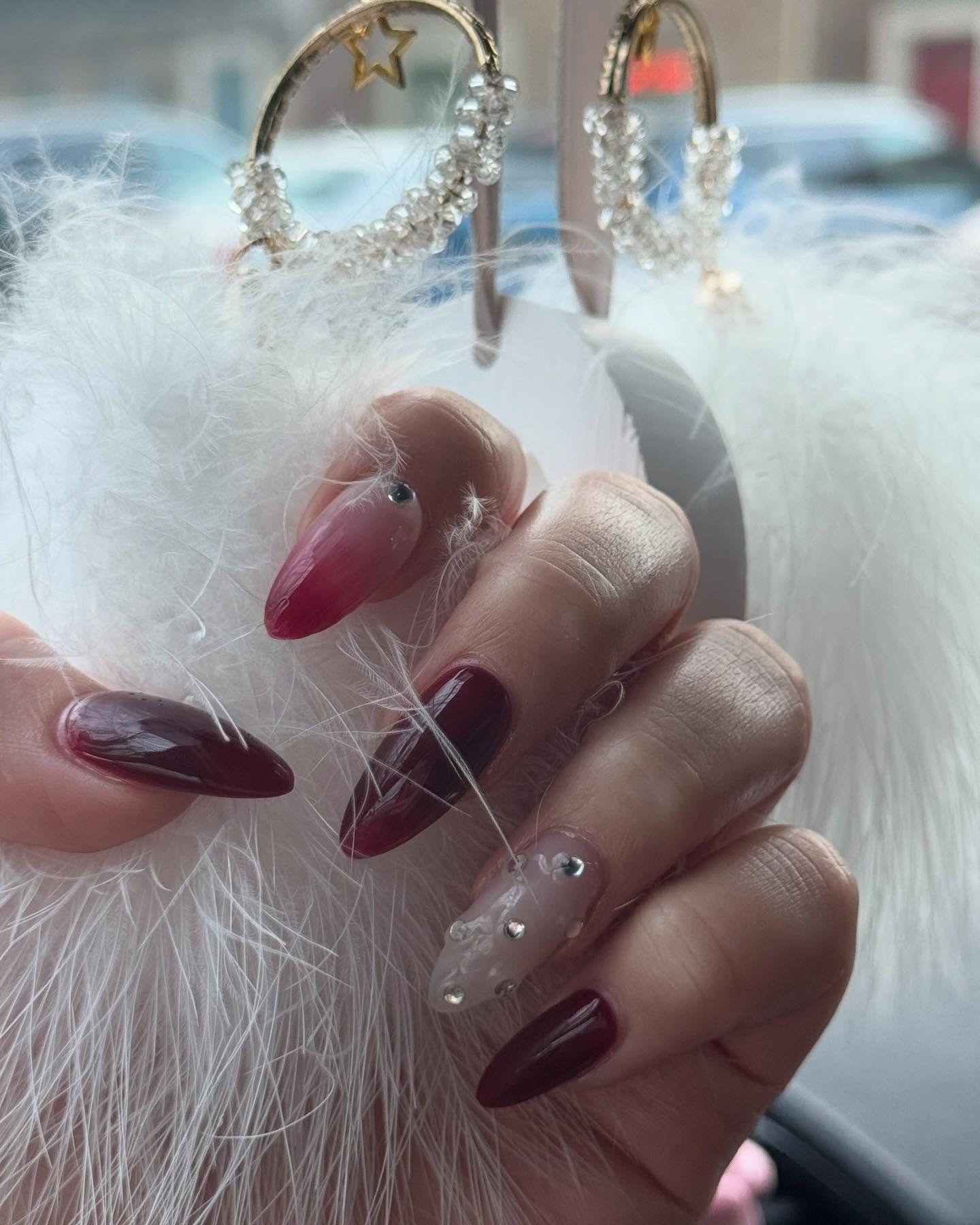 Hand holding a fluffy white accessory, showing off burgundy and nude-colored, bedazzled nails.